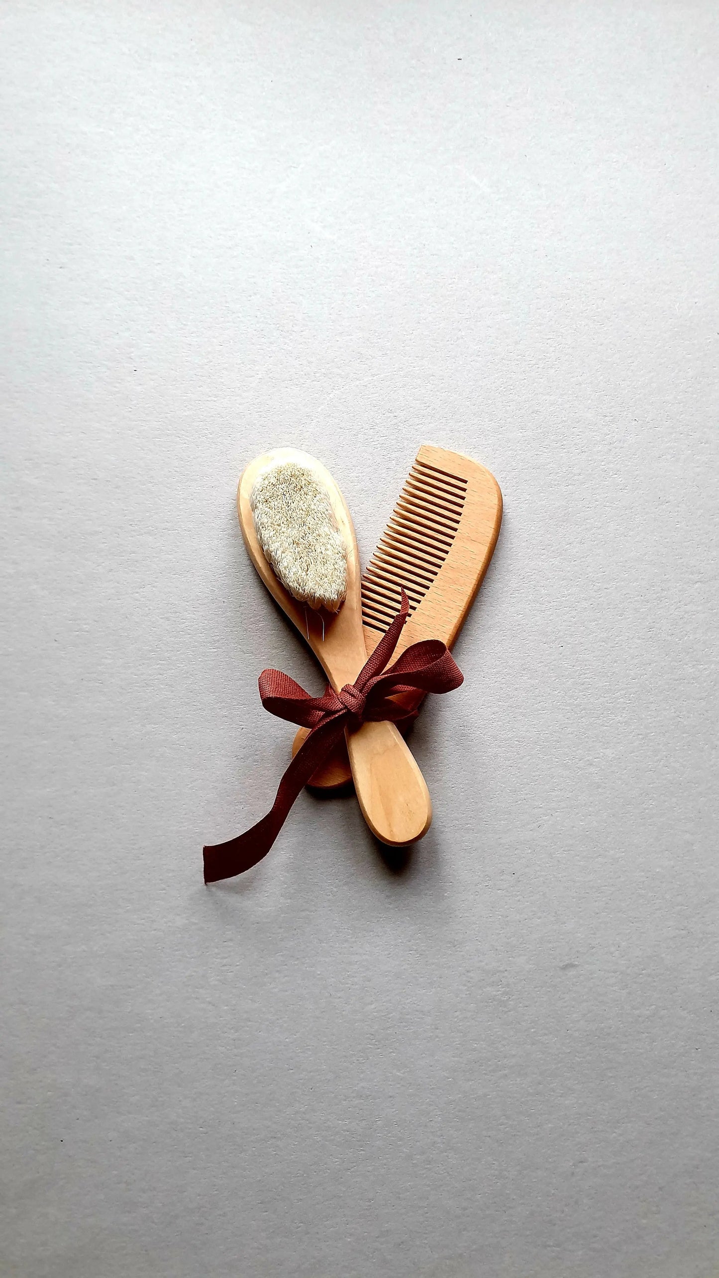 Wooden baby brush and comb set tied with a burgundy ribbon.
