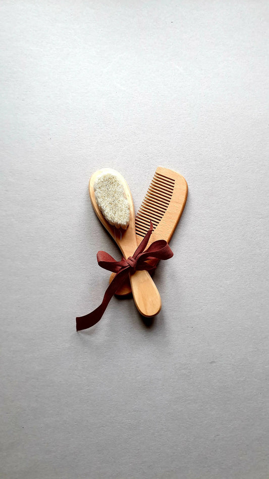 Wooden baby brush and comb set tied with a burgundy ribbon.