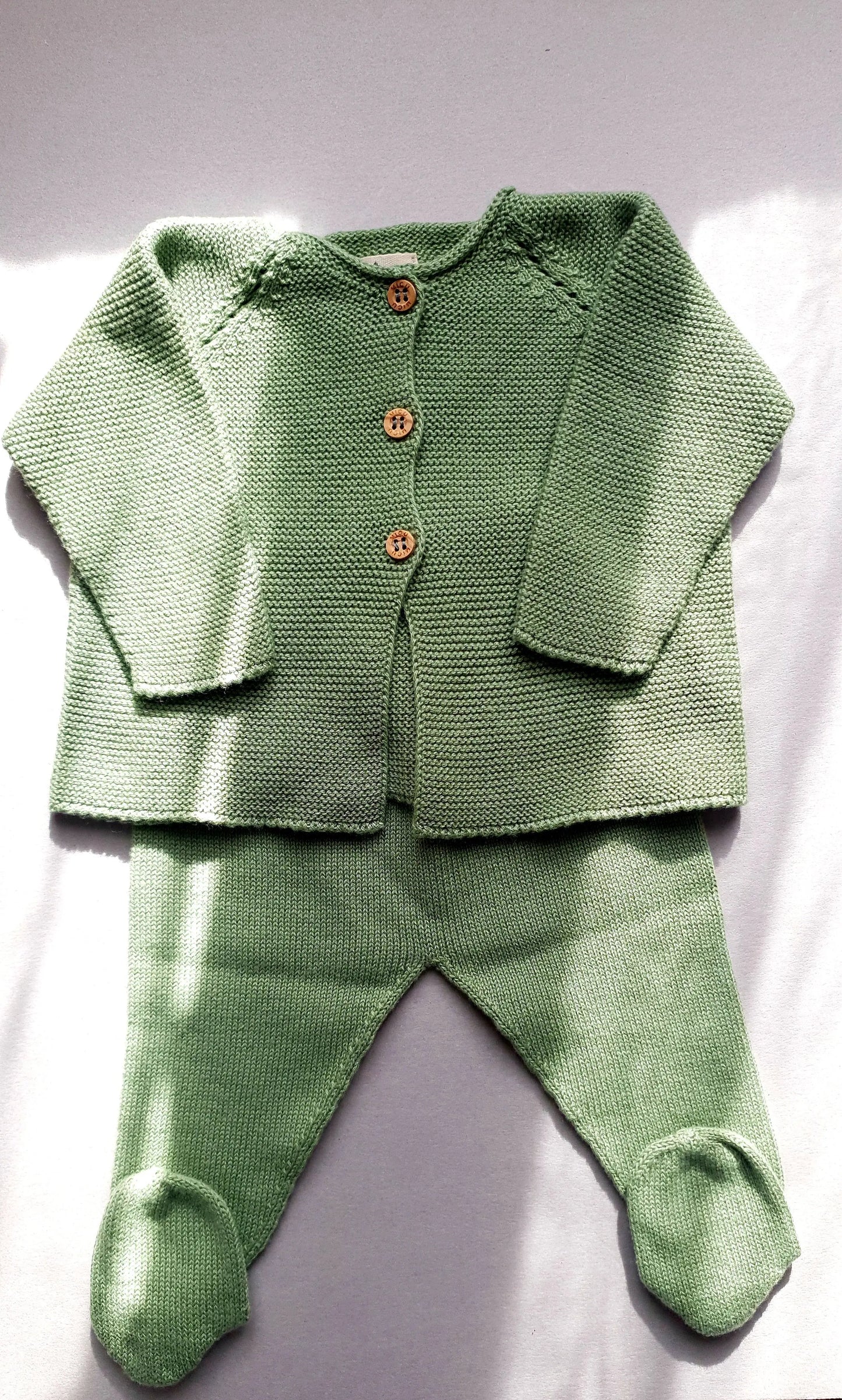 Green knitted baby outfit with long sleeves and buttons.