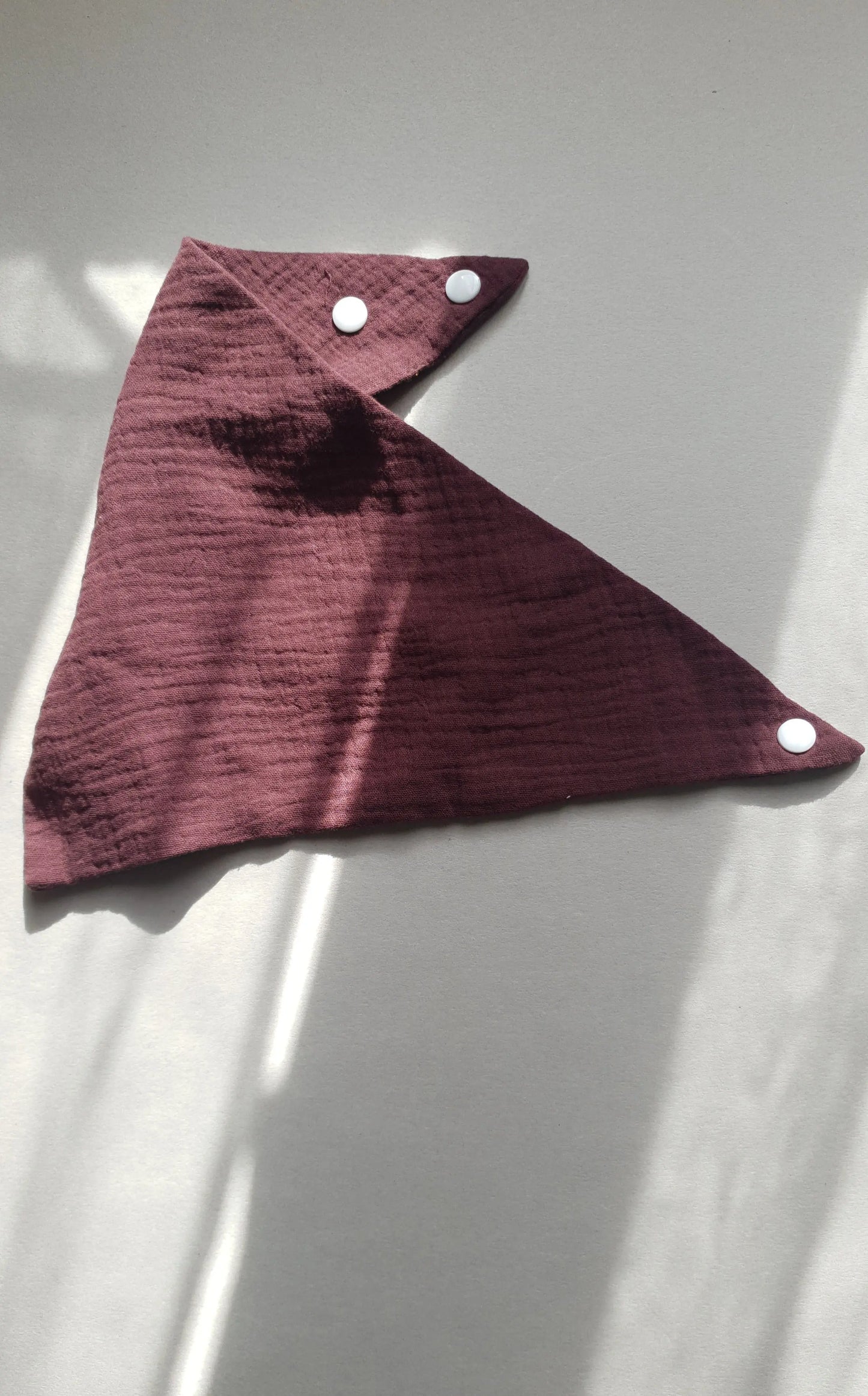 A dark burgundy napkin with three white snap buttons.