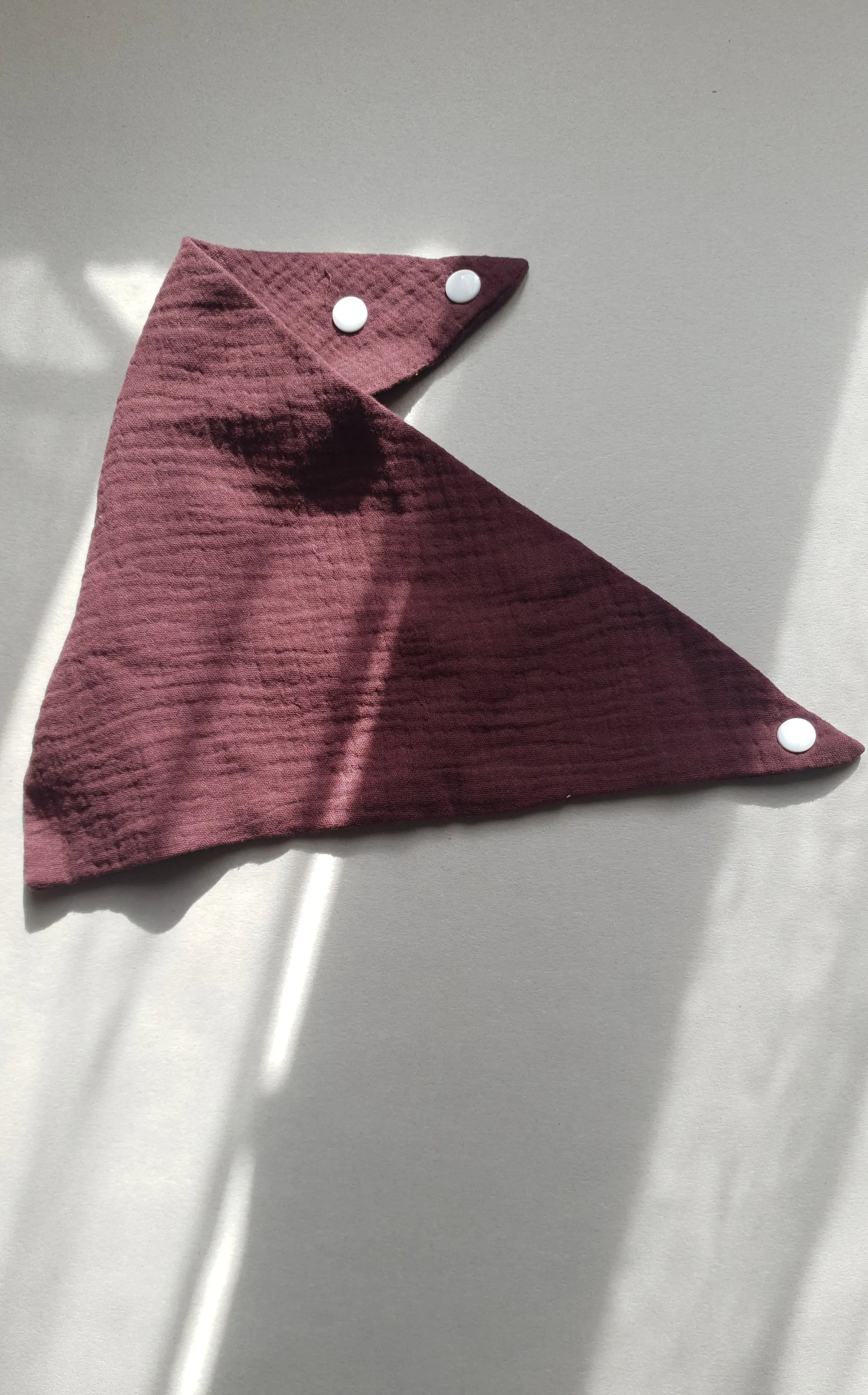 A dark burgundy napkin with three white snap buttons.