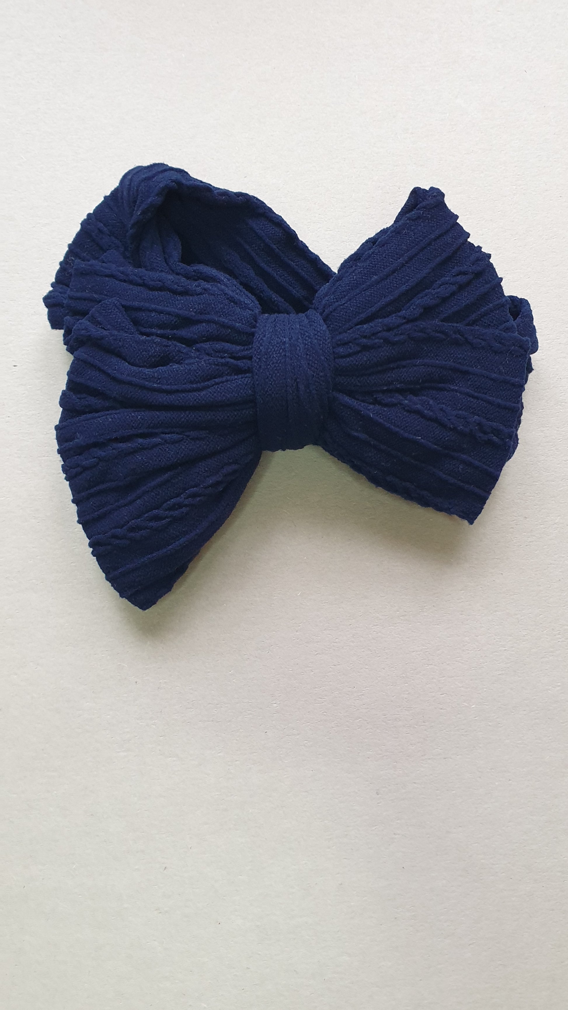 Dark blue textured fabric bow on a plain light background.
