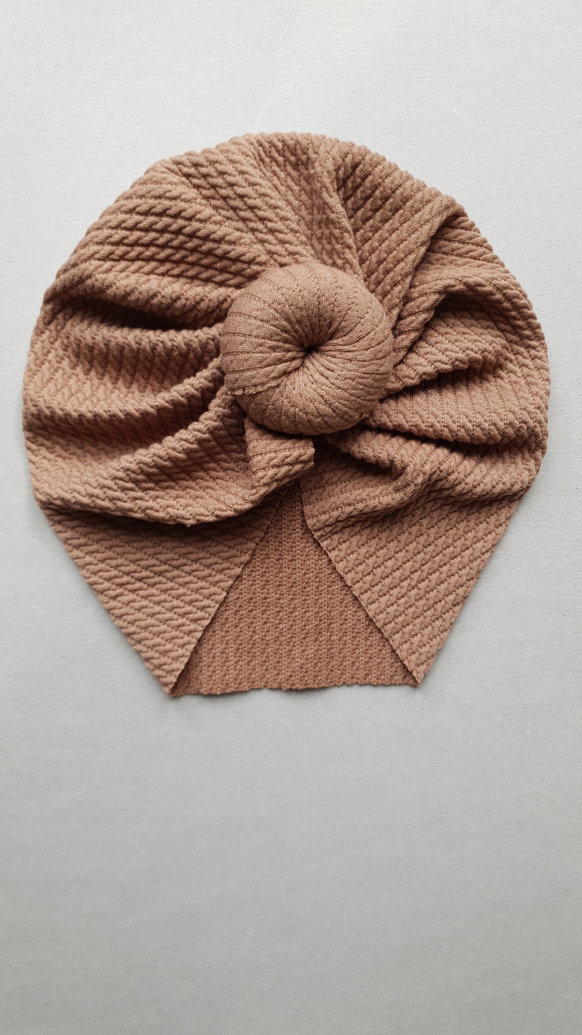 A textured brown fabric turban with intricate pleats.