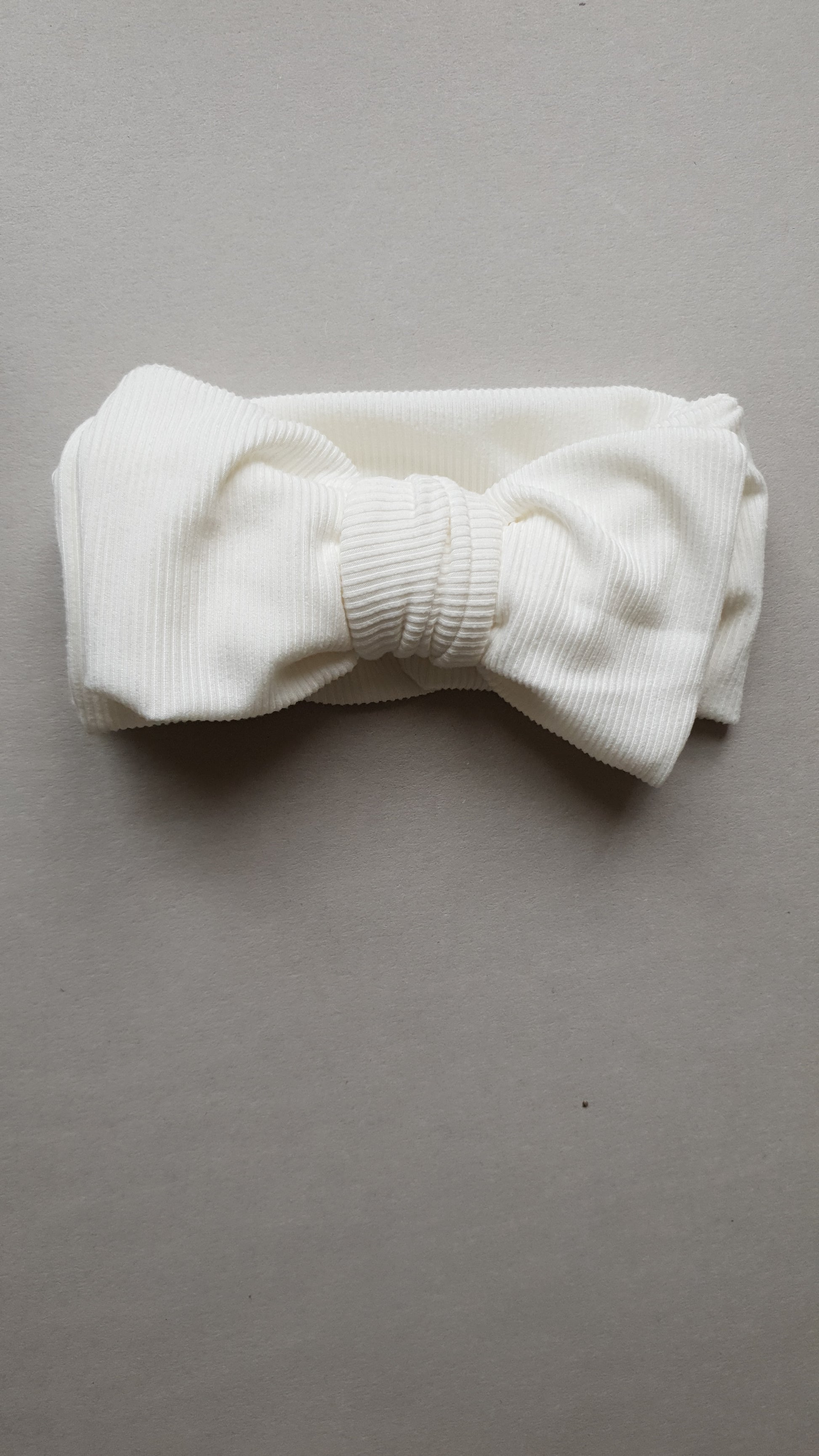 A white, textured fabric headband with a central bow.