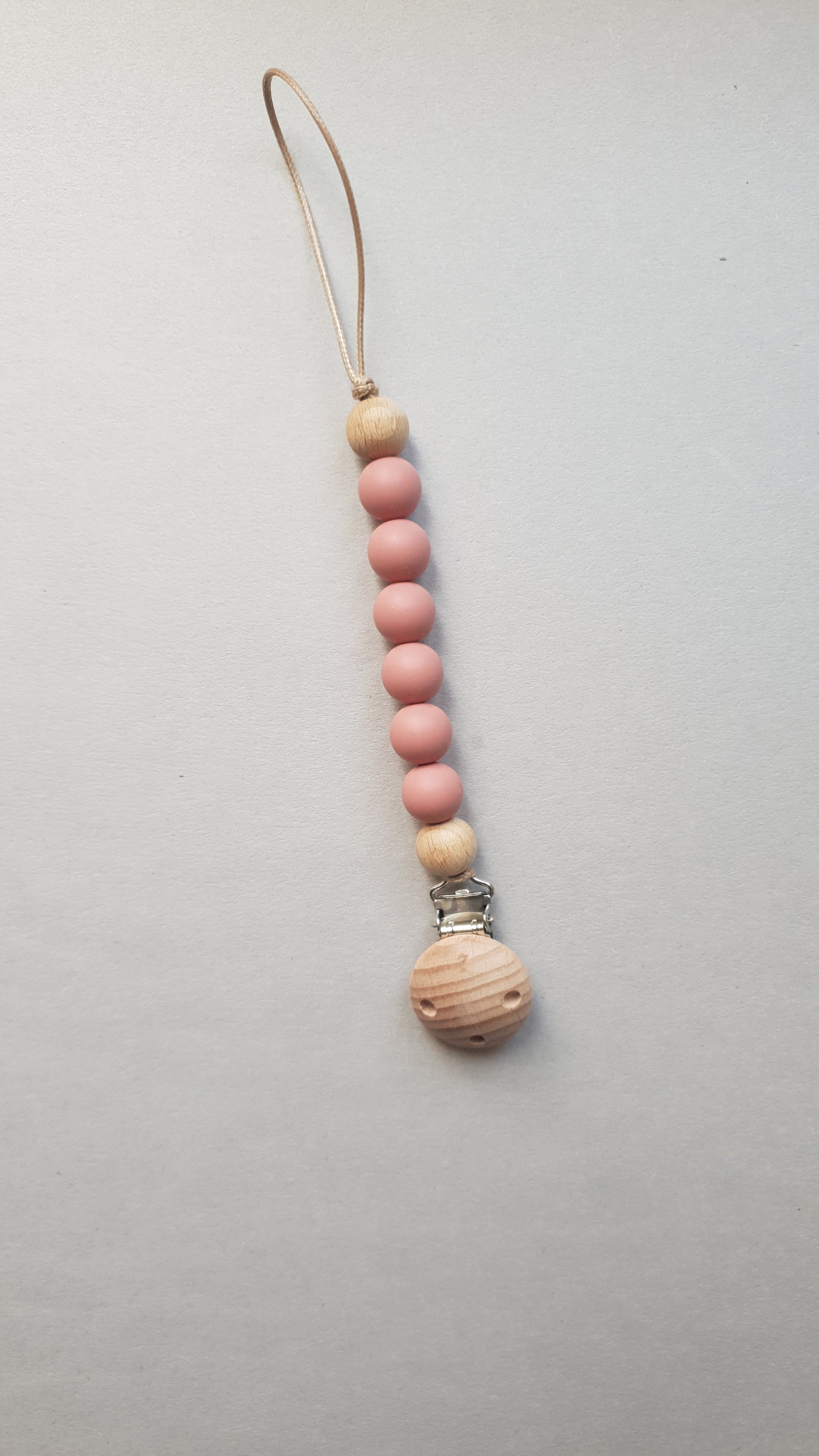 A pacifier clip with alternating light wood and pink beads.