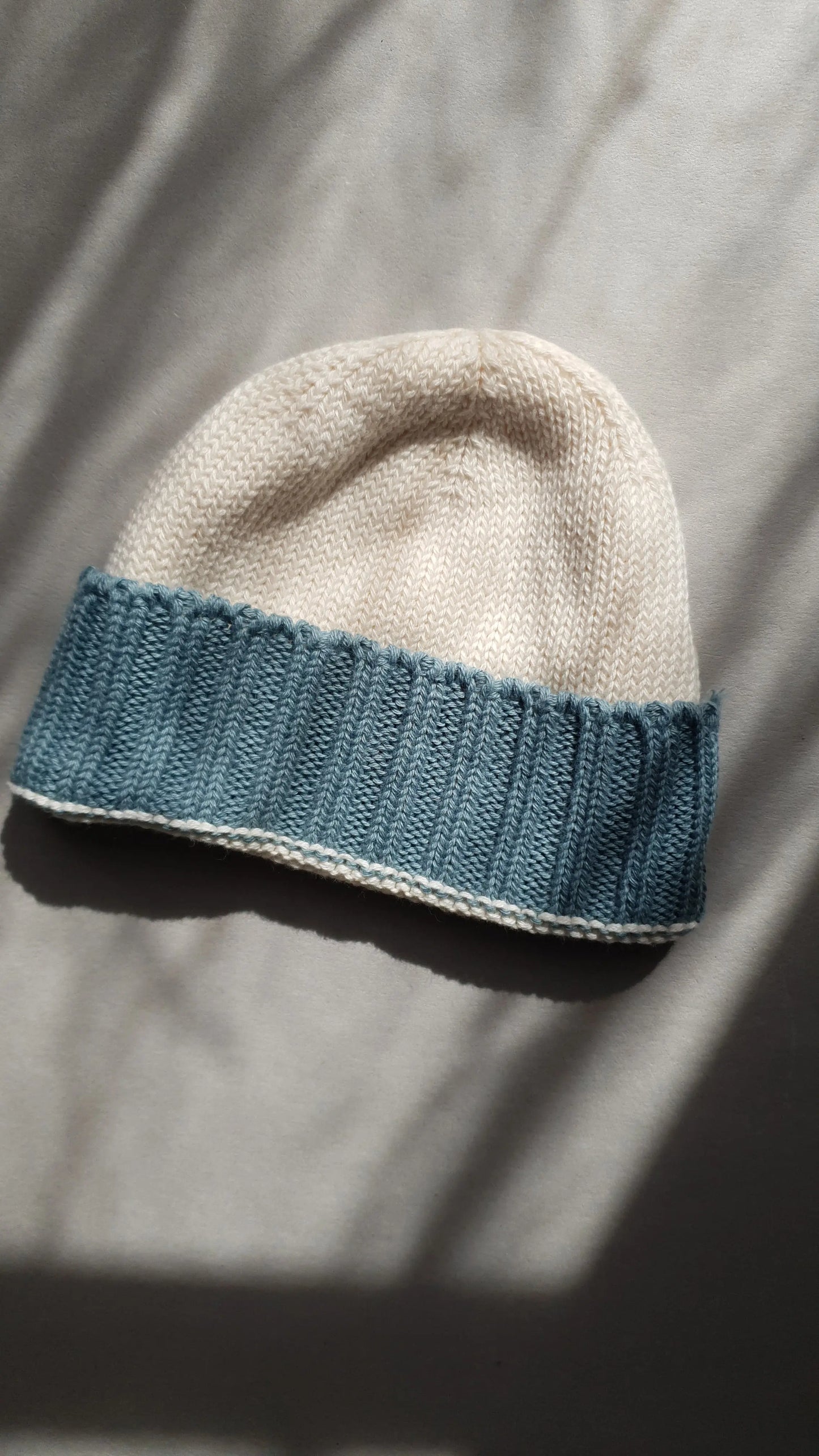 A cream-colored knit beanie with a light blue ribbed brim.