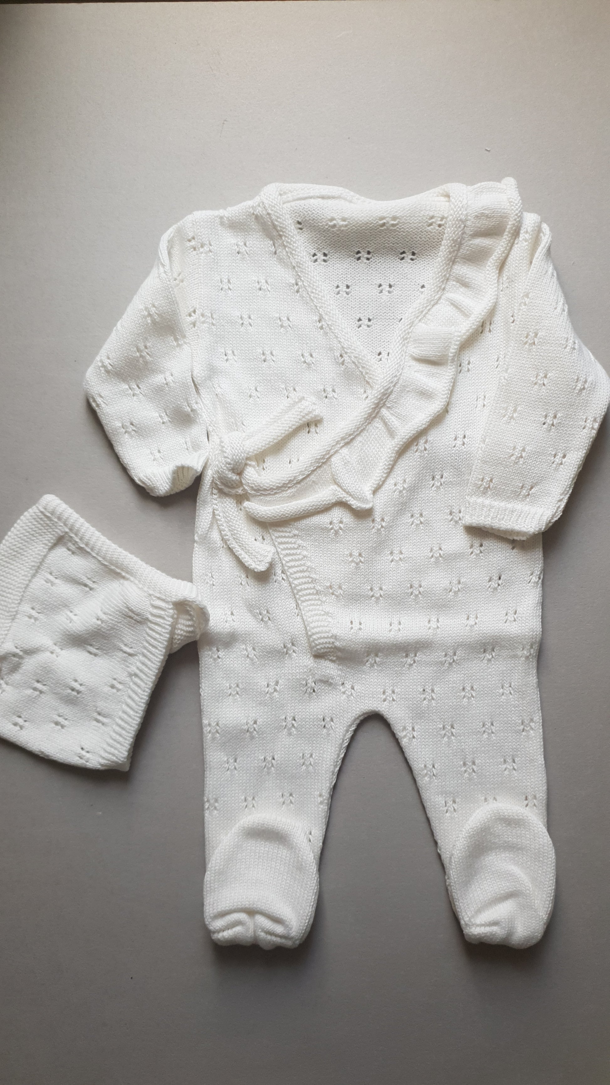 Cream-colored knitted baby outfit with a wrap-style top.