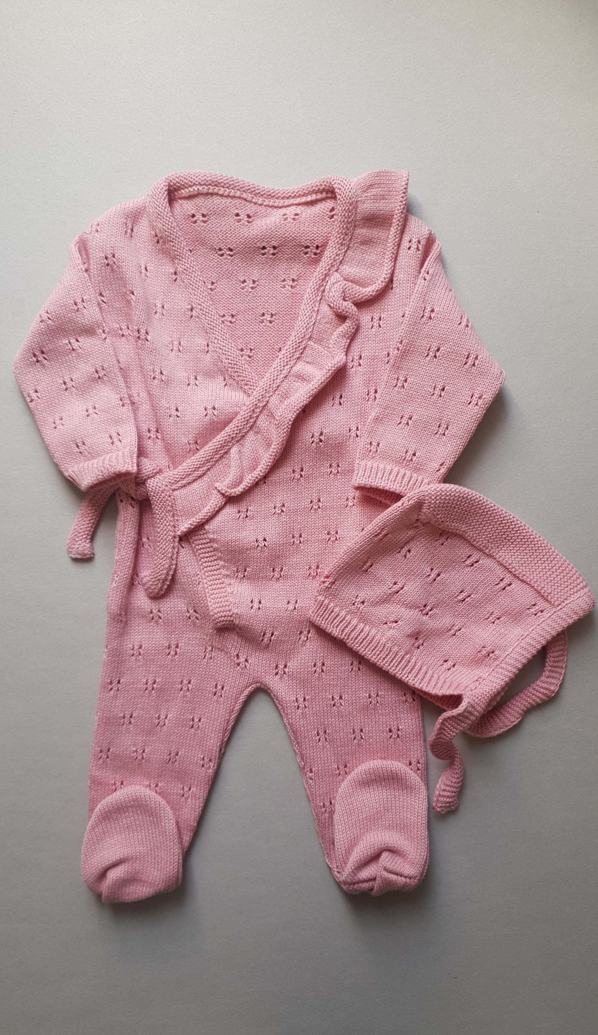 A soft pink knitted baby outfit with delicate patterns.