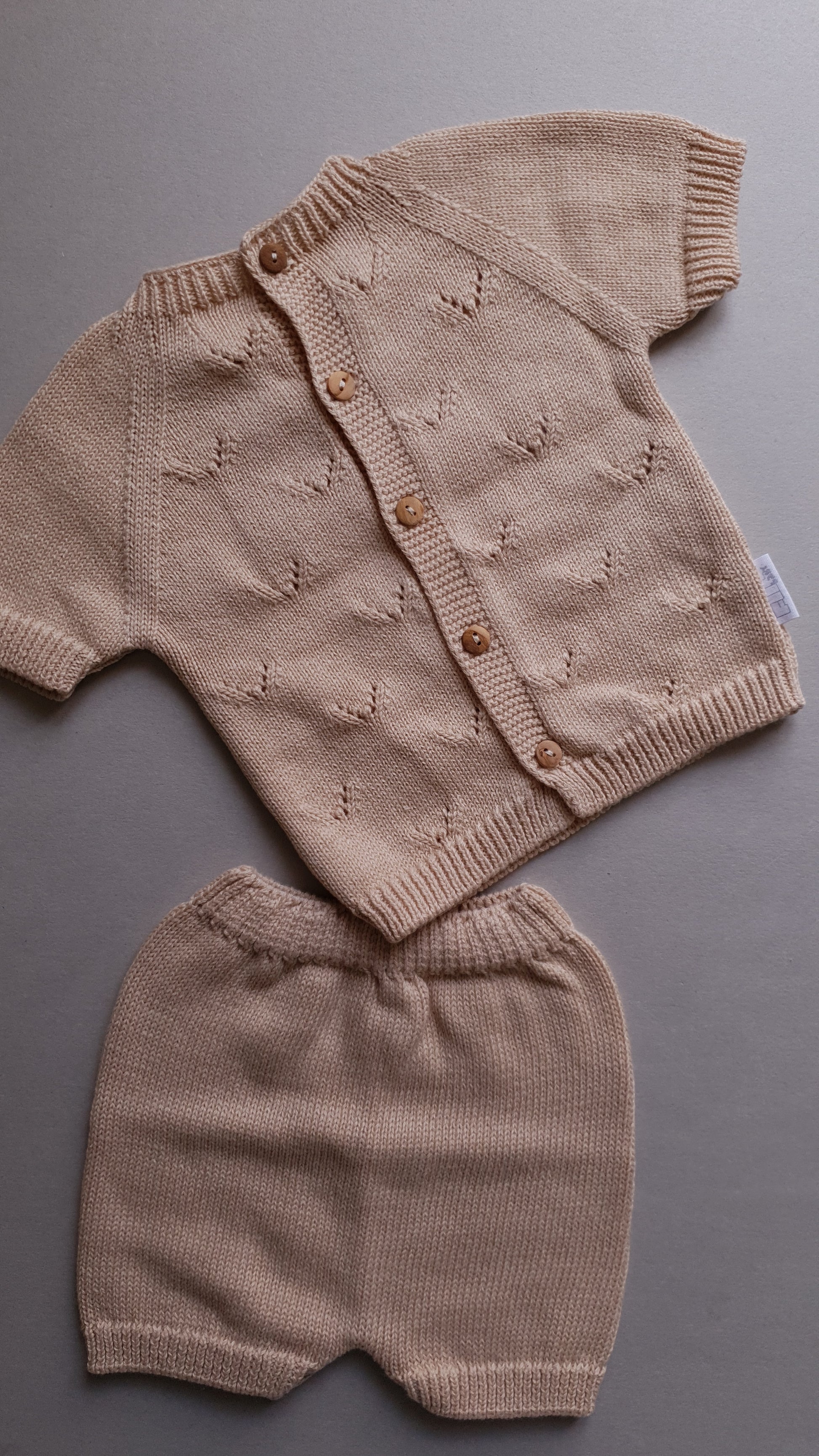 Beige baby outfit with a short-sleeved, button-up cardigan.