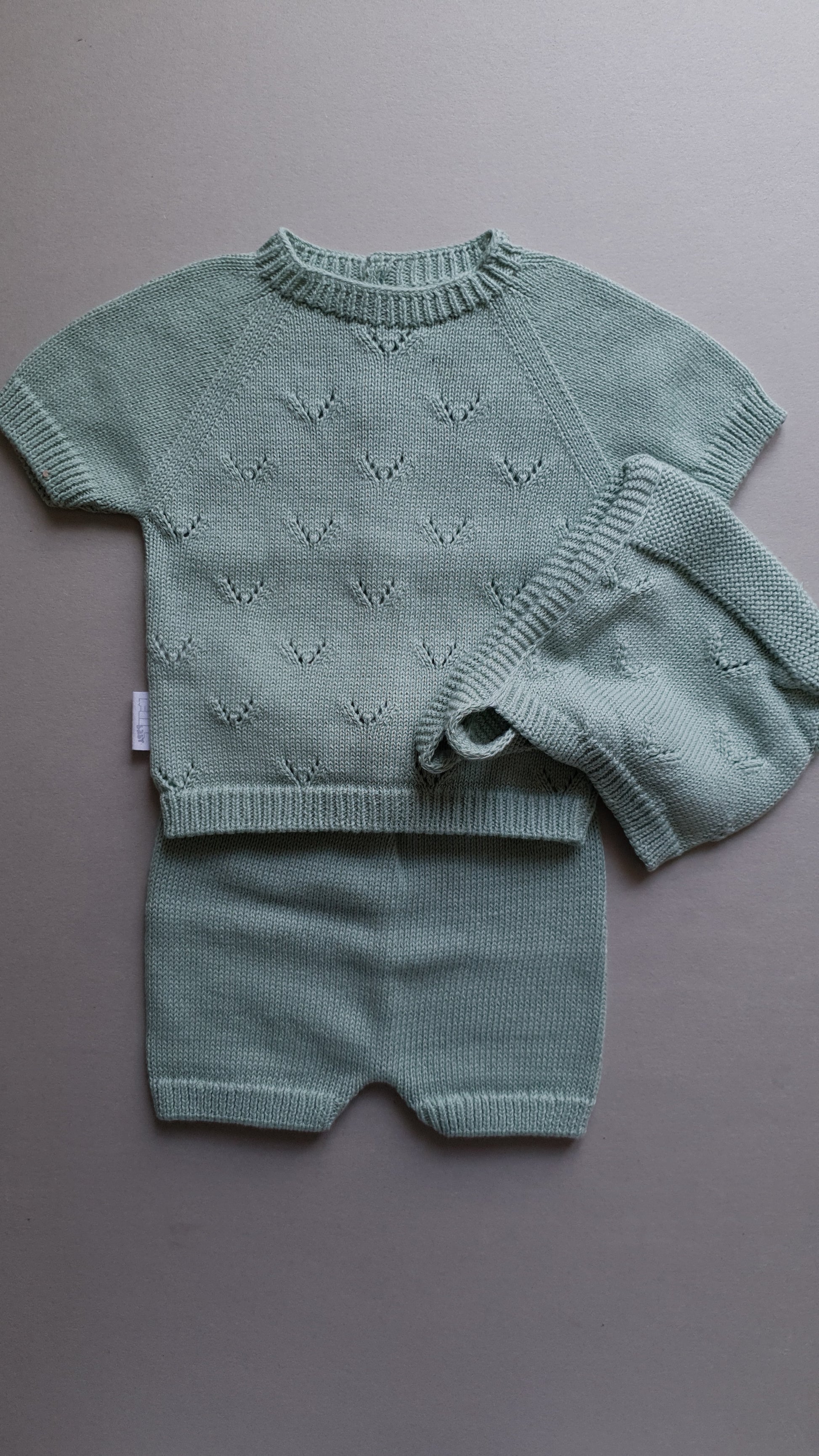A soft, light green baby knit outfit set on a gray background.