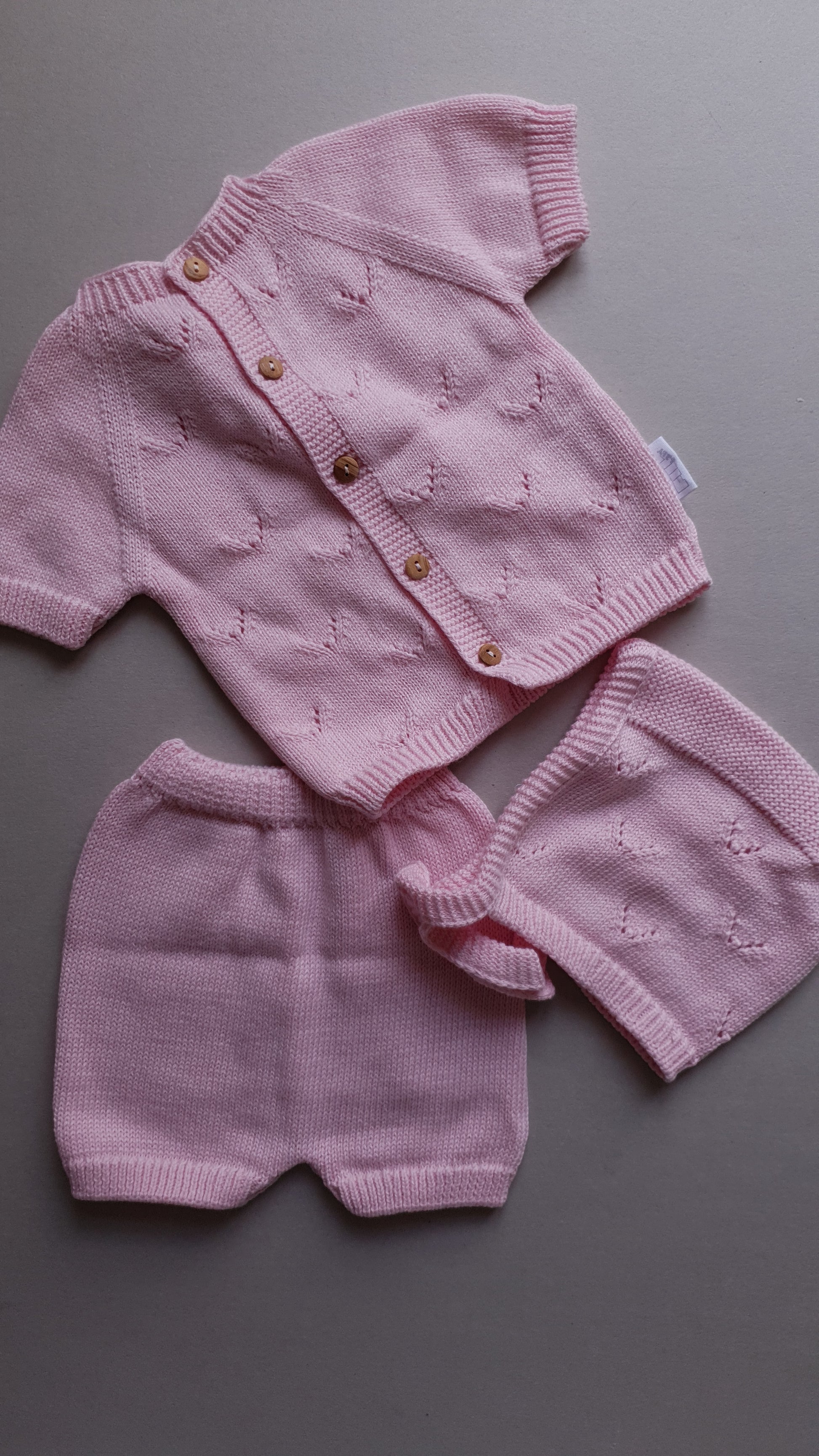 Pink knitted baby outfit with a short-sleeved cardigan.