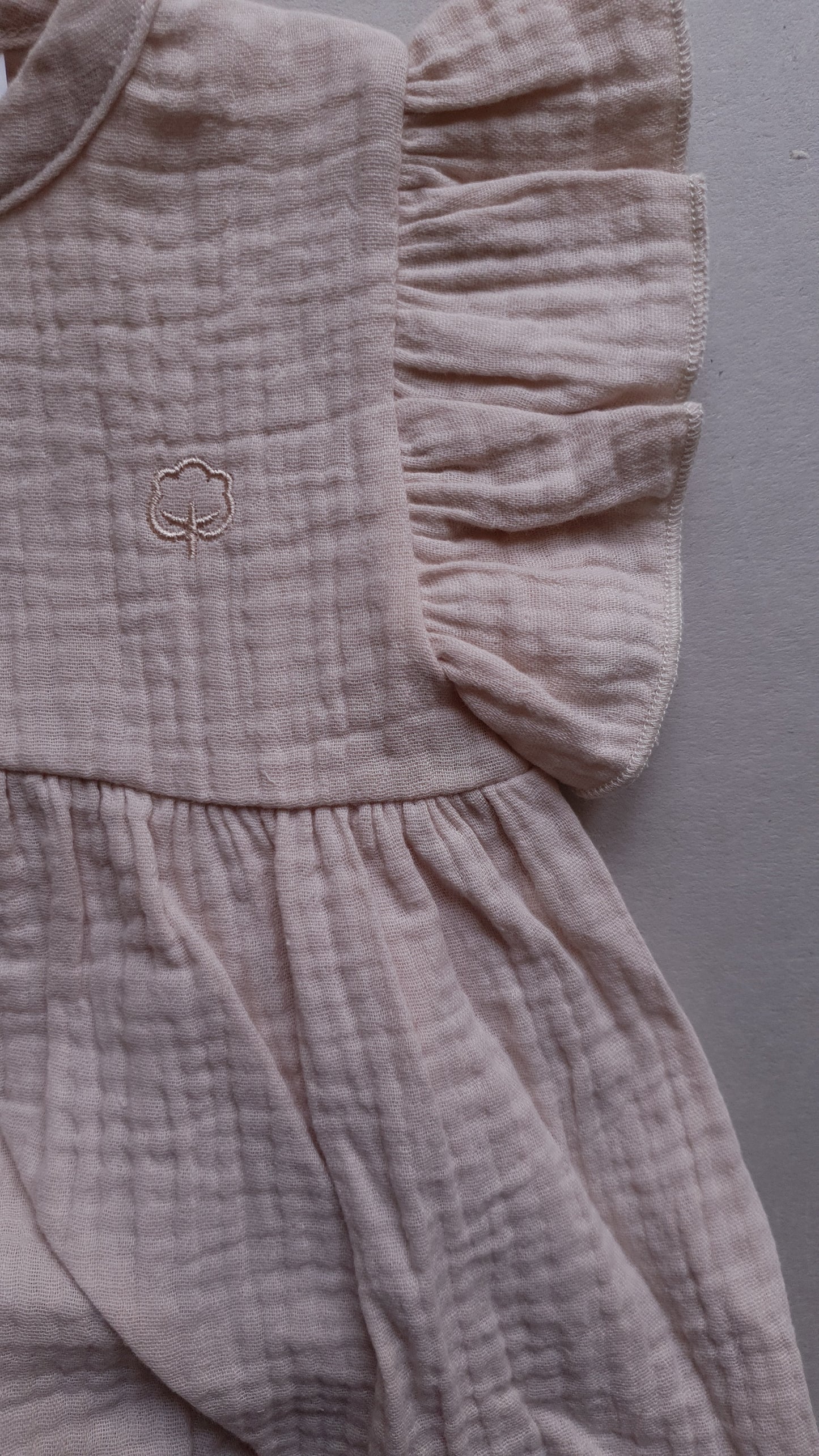 A soft pink dress with ruffled sleeves, with a tree symbol.