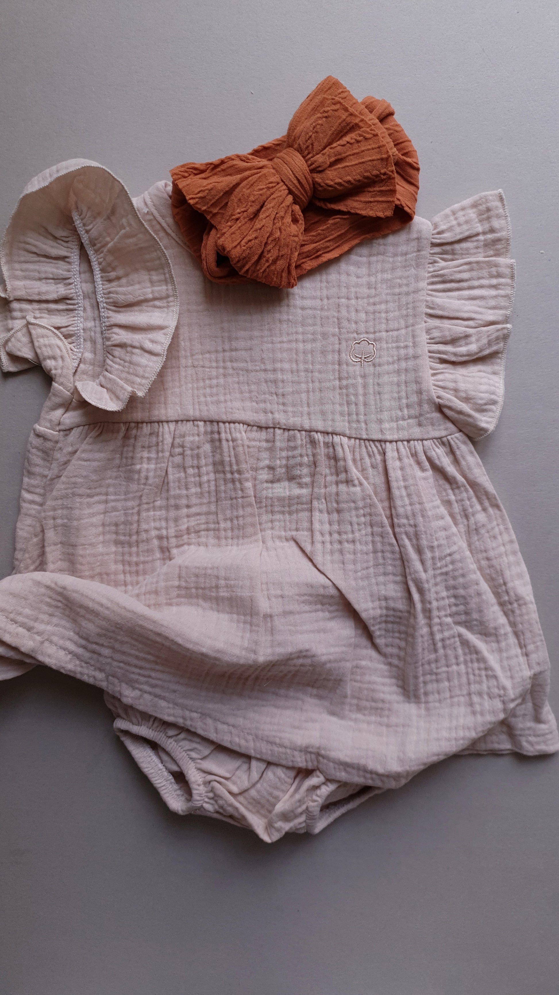 A soft, pale pink baby romper with a brown bow.