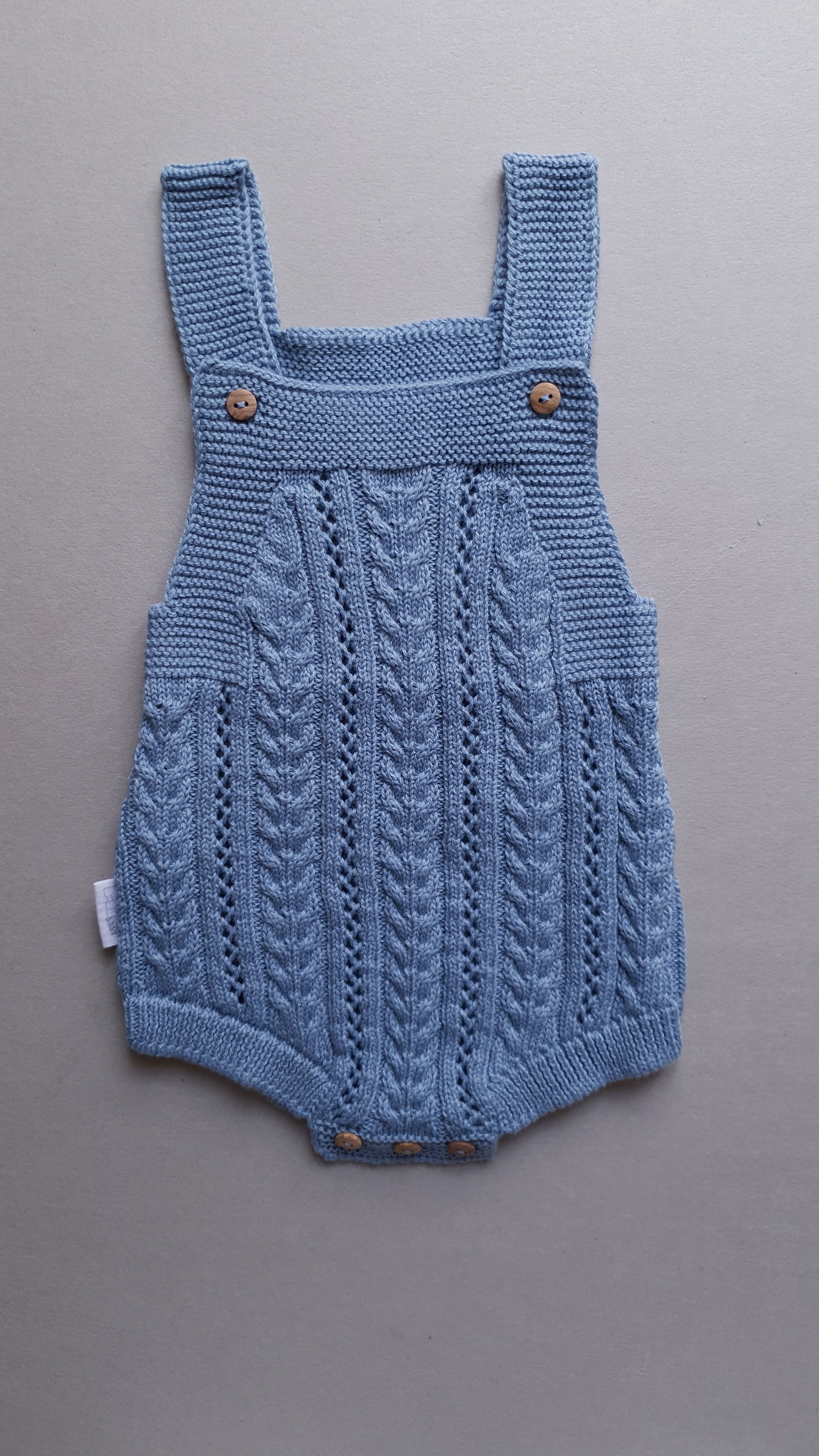 Blue baby romper with wooden buttons on straps.