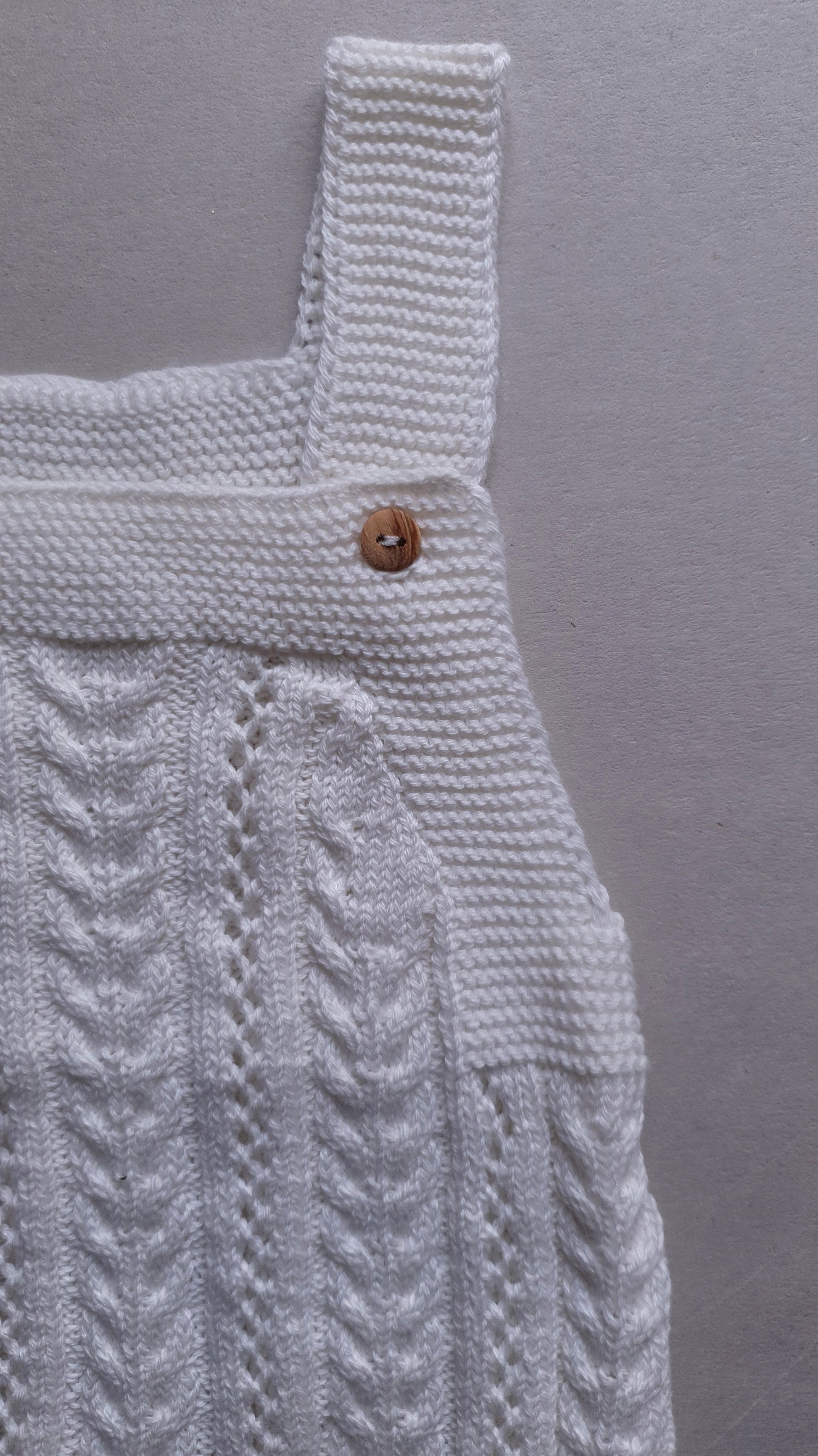 A white knitted fabric with a pattern and a wooden button.