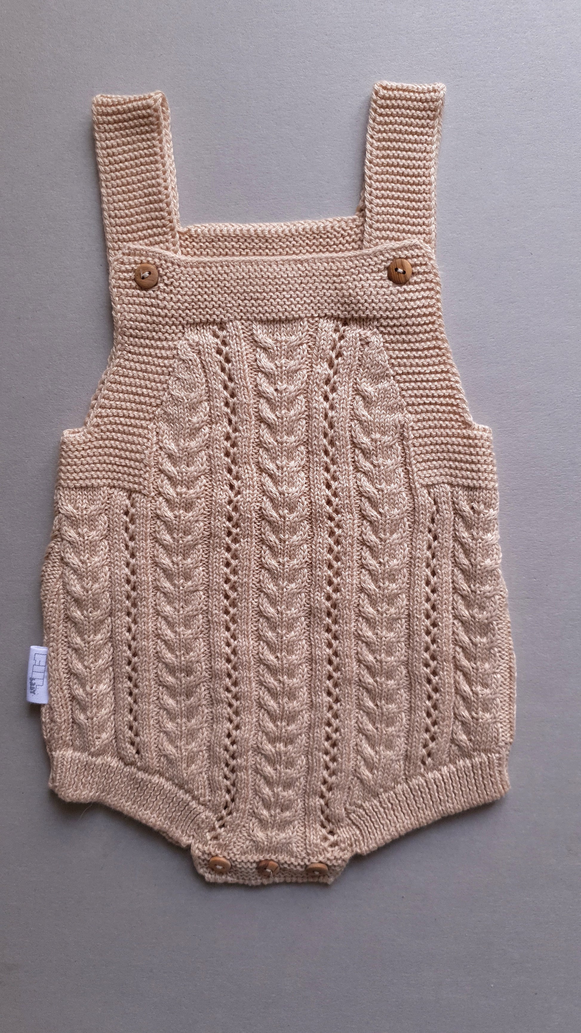 Beige baby romper with a knit pattern and buttoned straps.