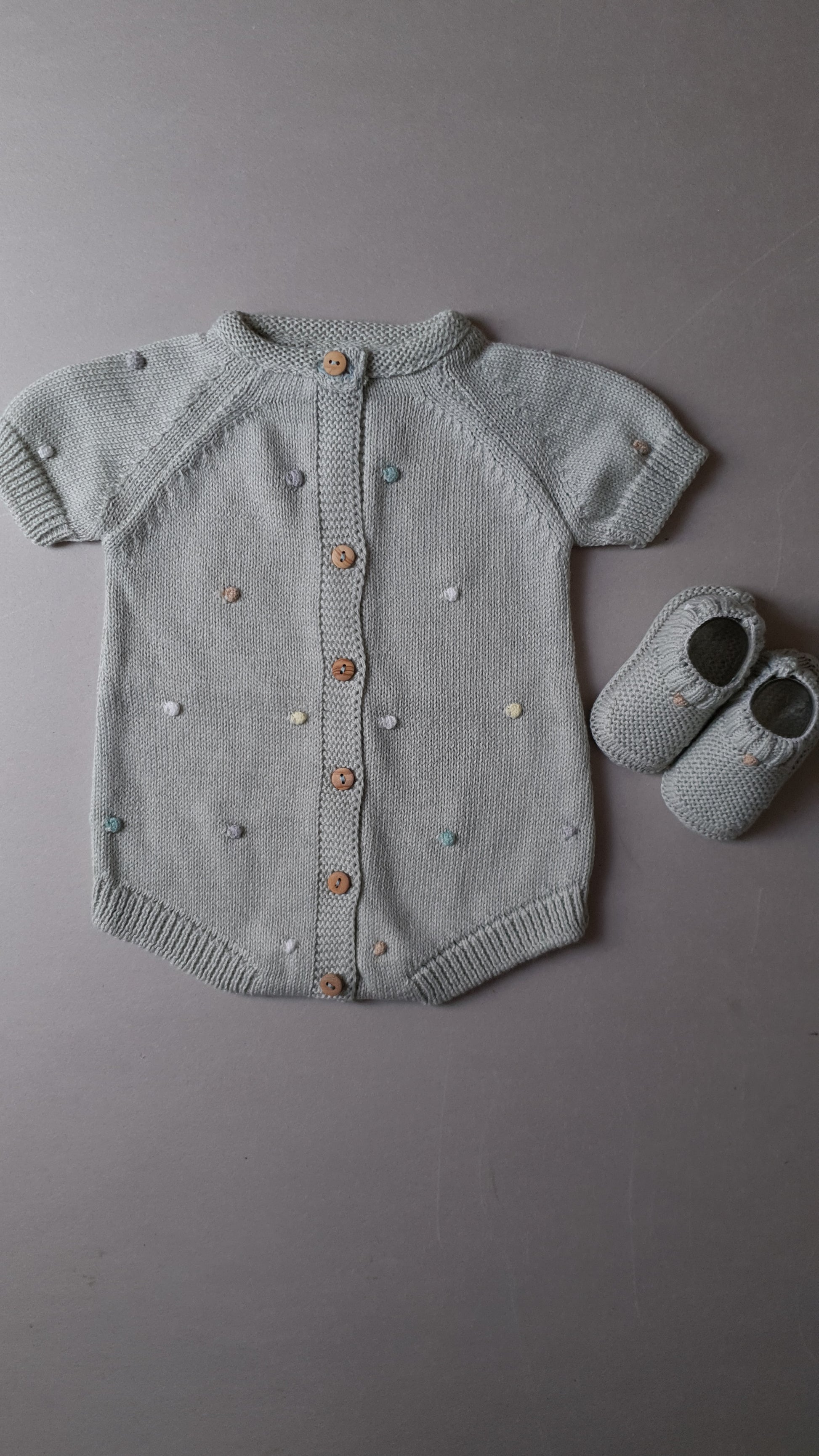 Gray knitted baby romper with buttons and colored dots.