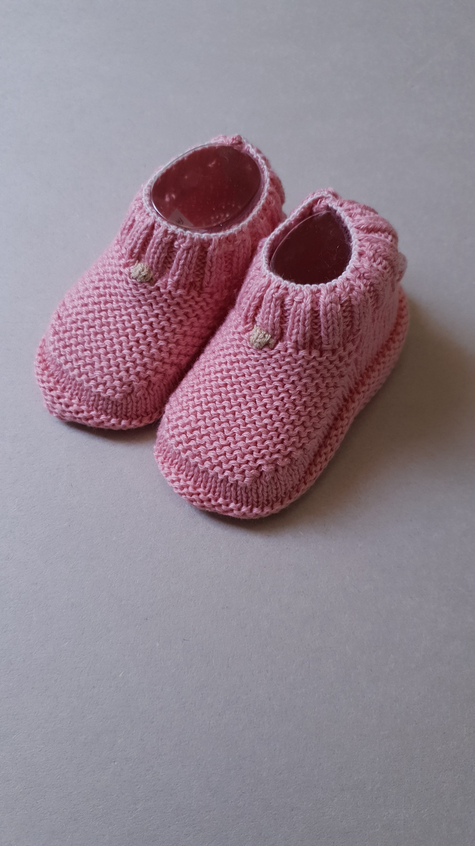 Two pink knitted baby boots are placed side by side.