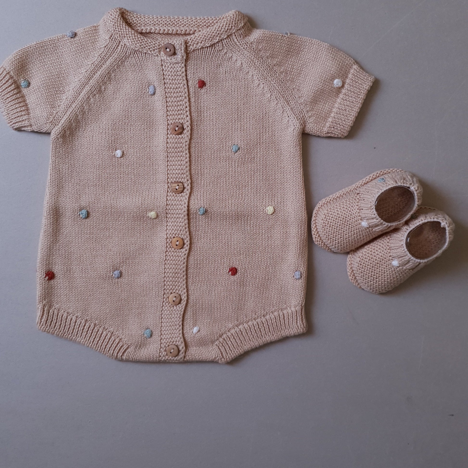 Beige knitted baby romper with multicolored embroidered dots.