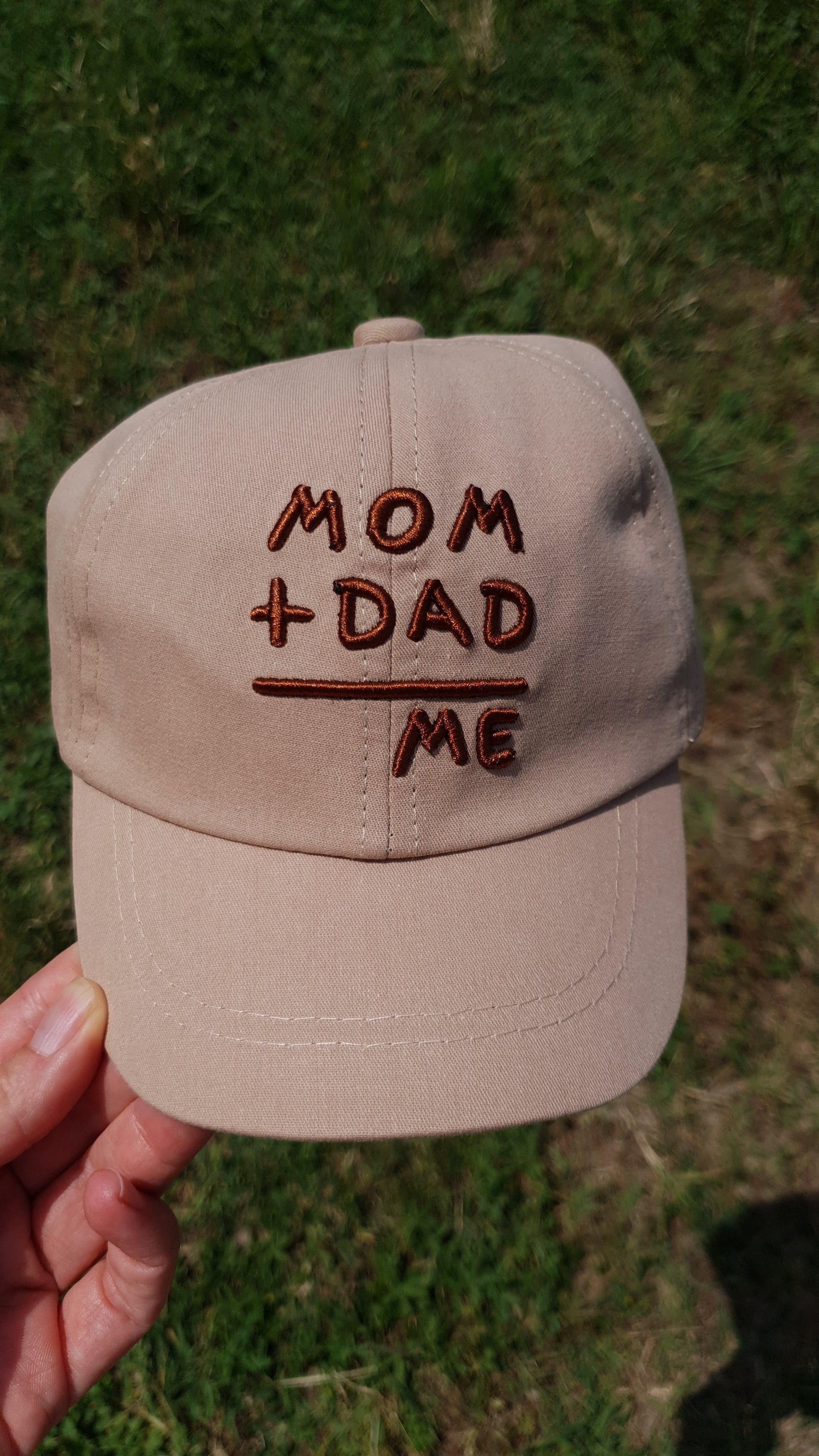 A baseball cap with "Mom + Dad = Me" in brown letters.