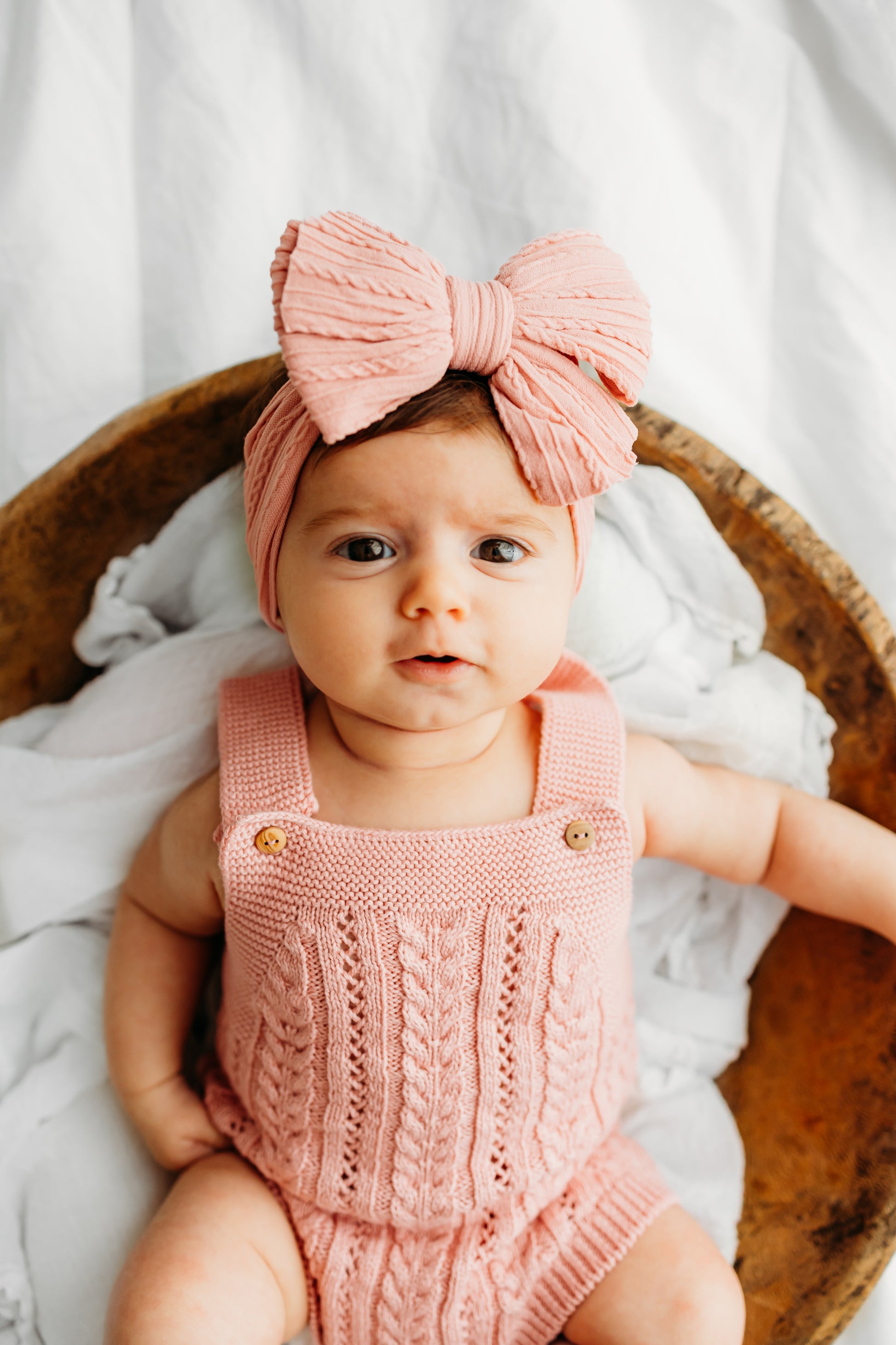 A baby wearing a pink outfit and a large bow headband.