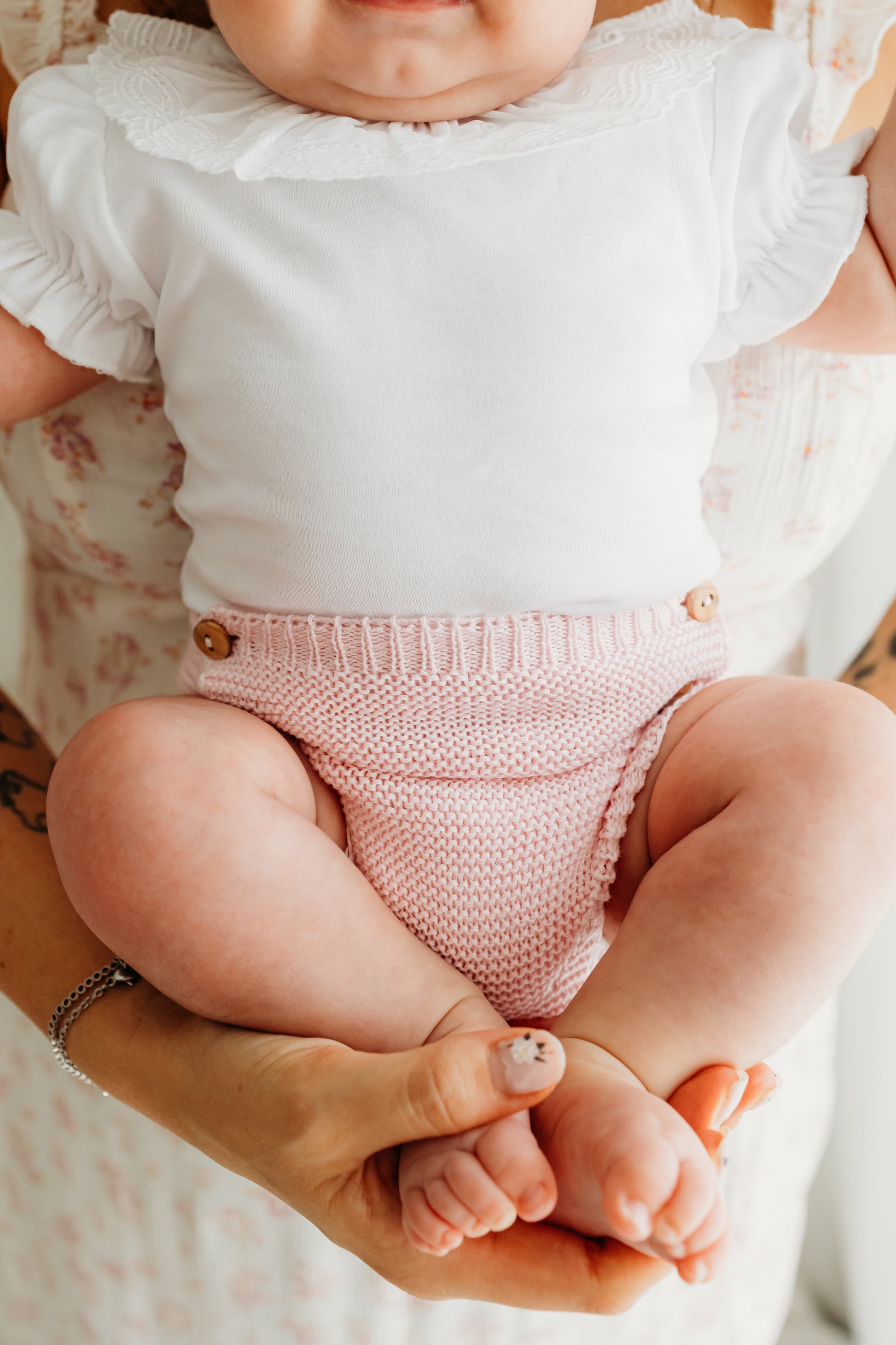 A baby in a white top and a pink knitted diaper.
