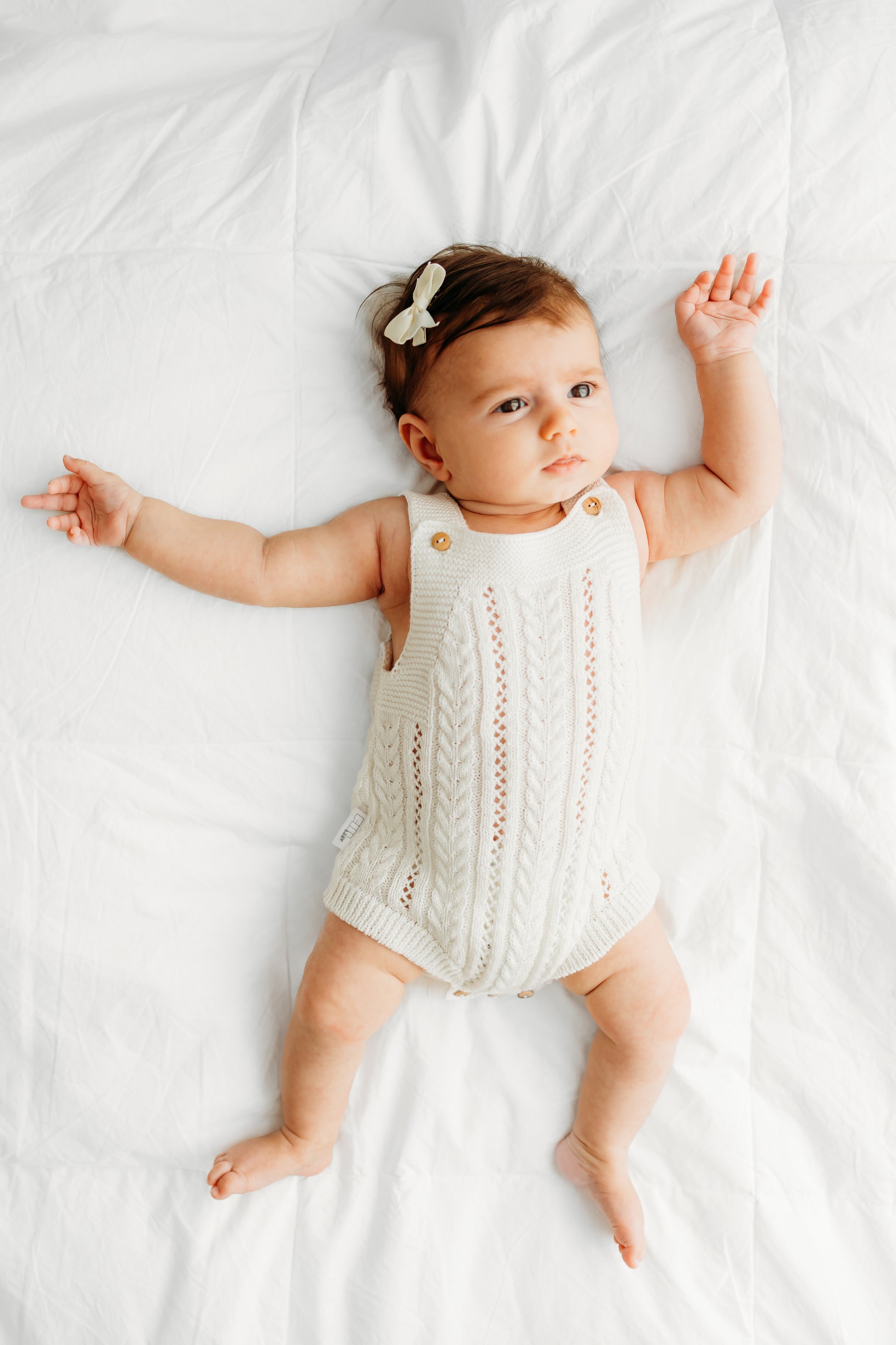 Baby wearing a cream knitted romper and a small bow.