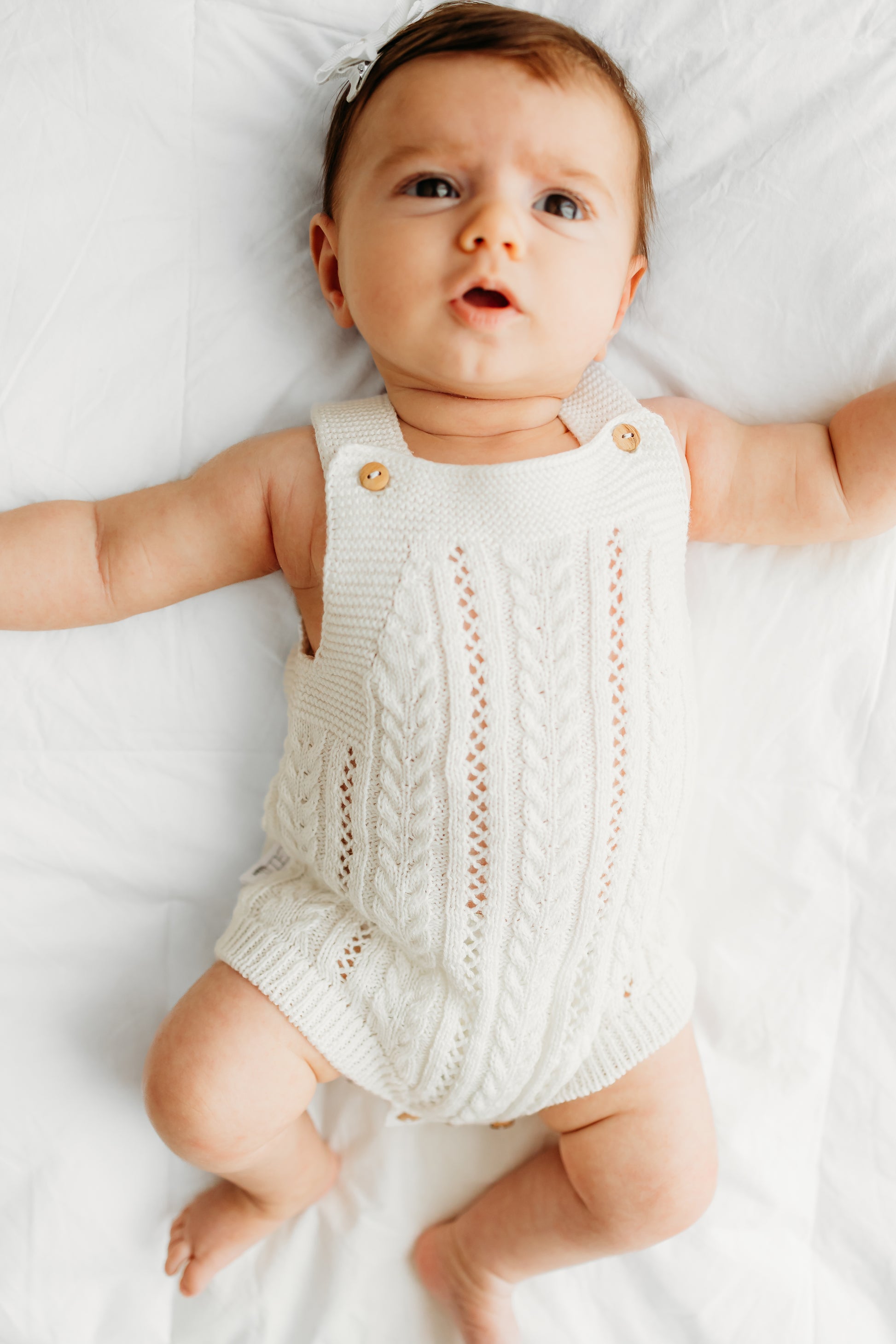 Baby is wearing a knitted white romper with cable patterns.