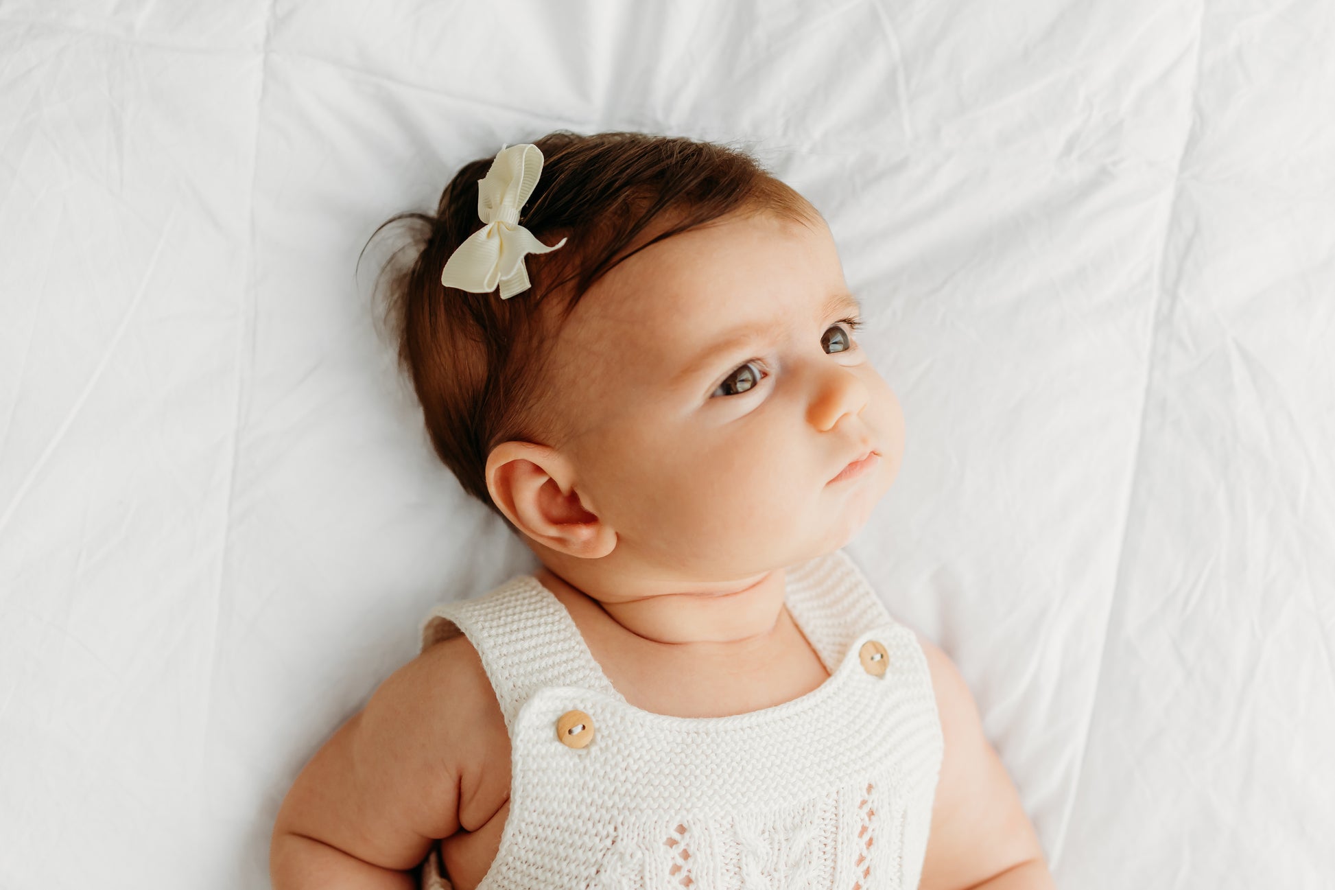 A baby wearing a cream knitted outfit with wooden buttons.