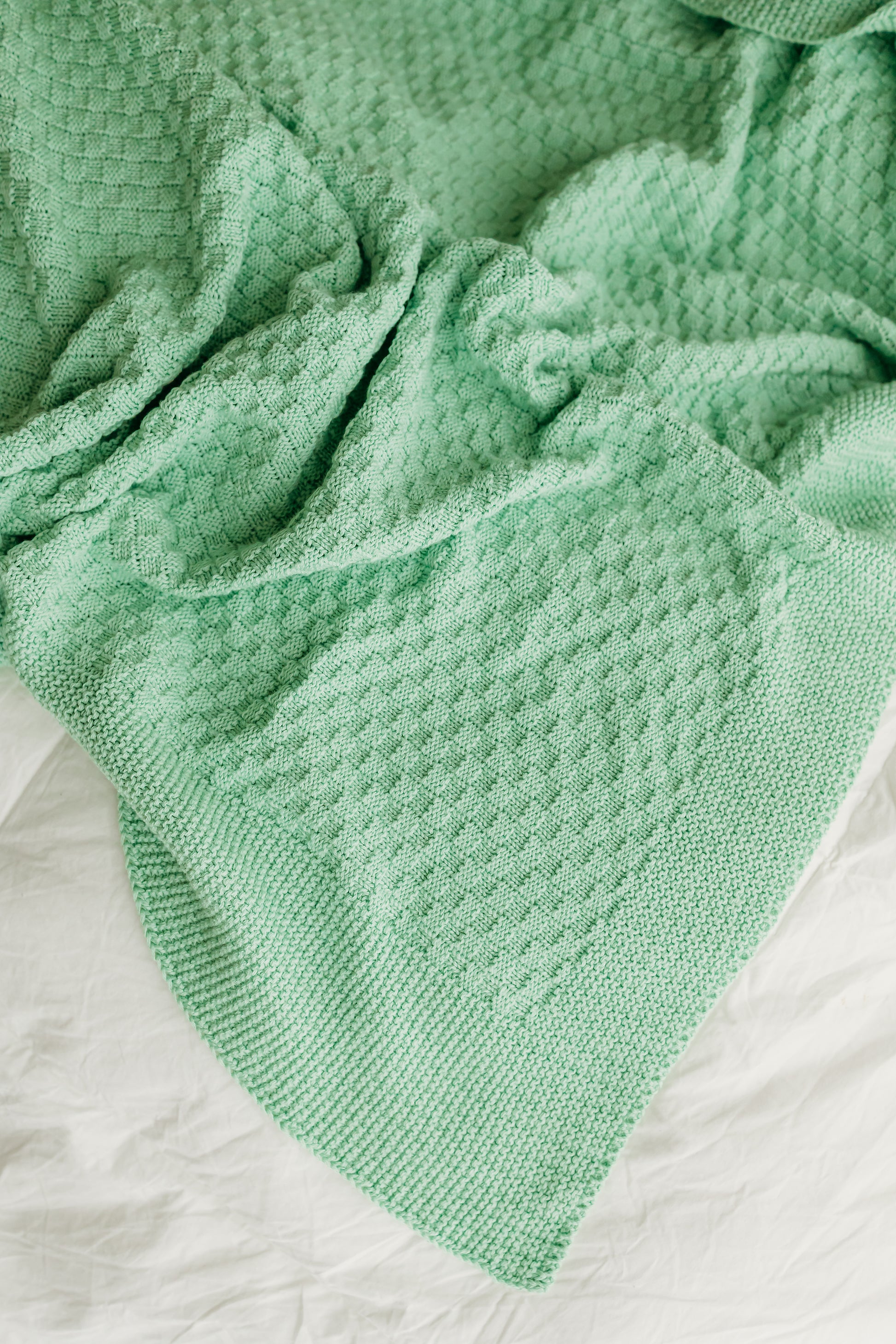 A soft, mint-green knitted blanket with a textured pattern.