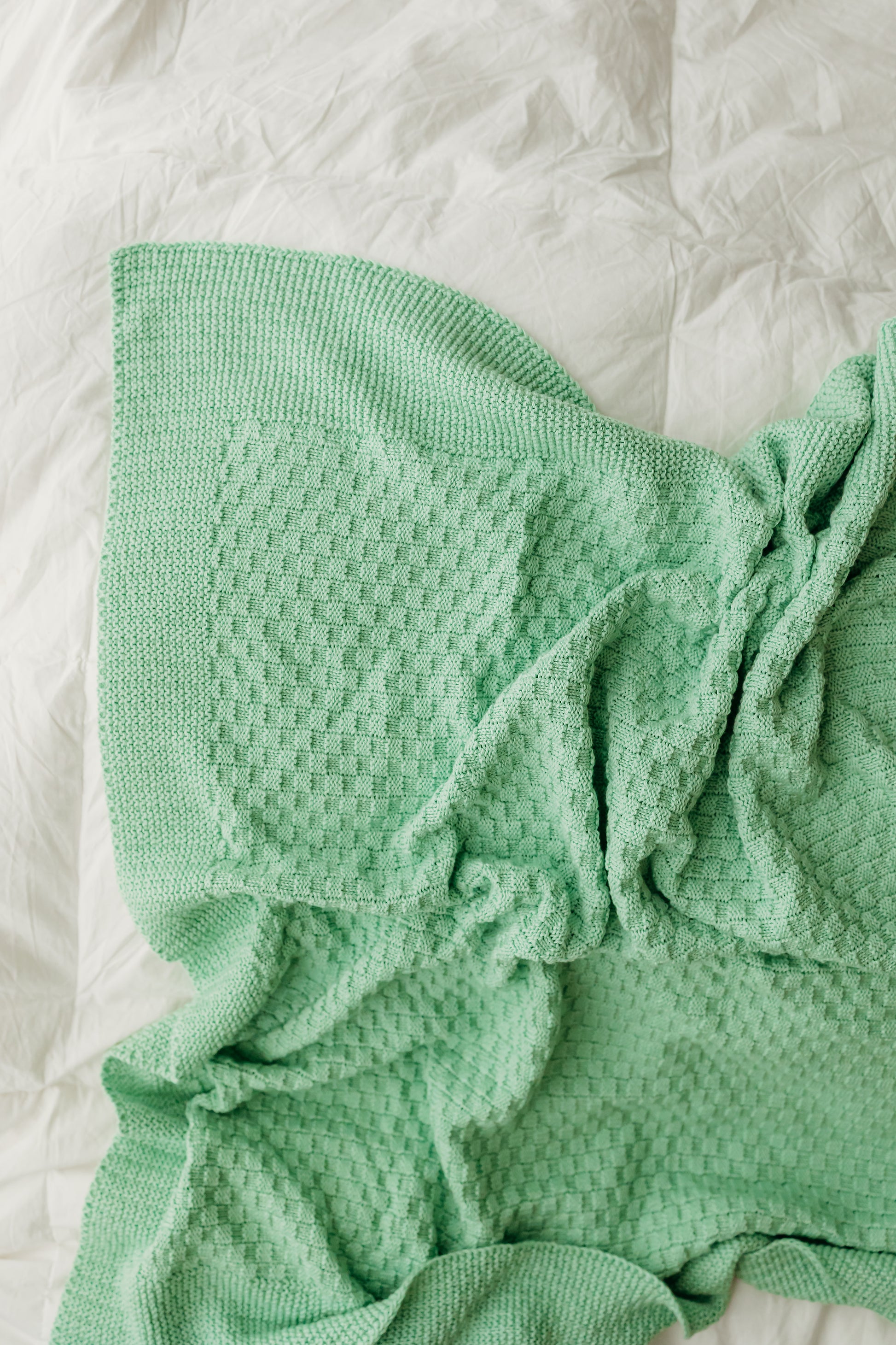 A mint-green blanket crumpled on a white sheet.