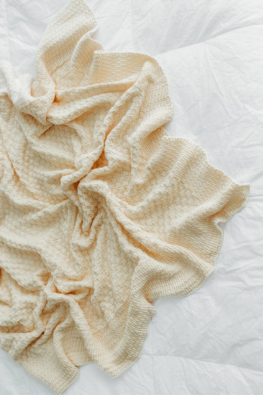 A crumpled beige textured blanket lies on a bedspread.