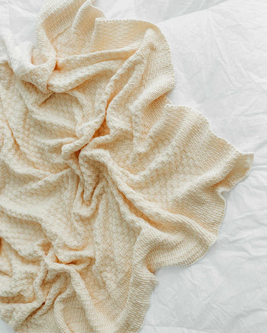 A crumpled beige textured blanket lies on a bedspread.