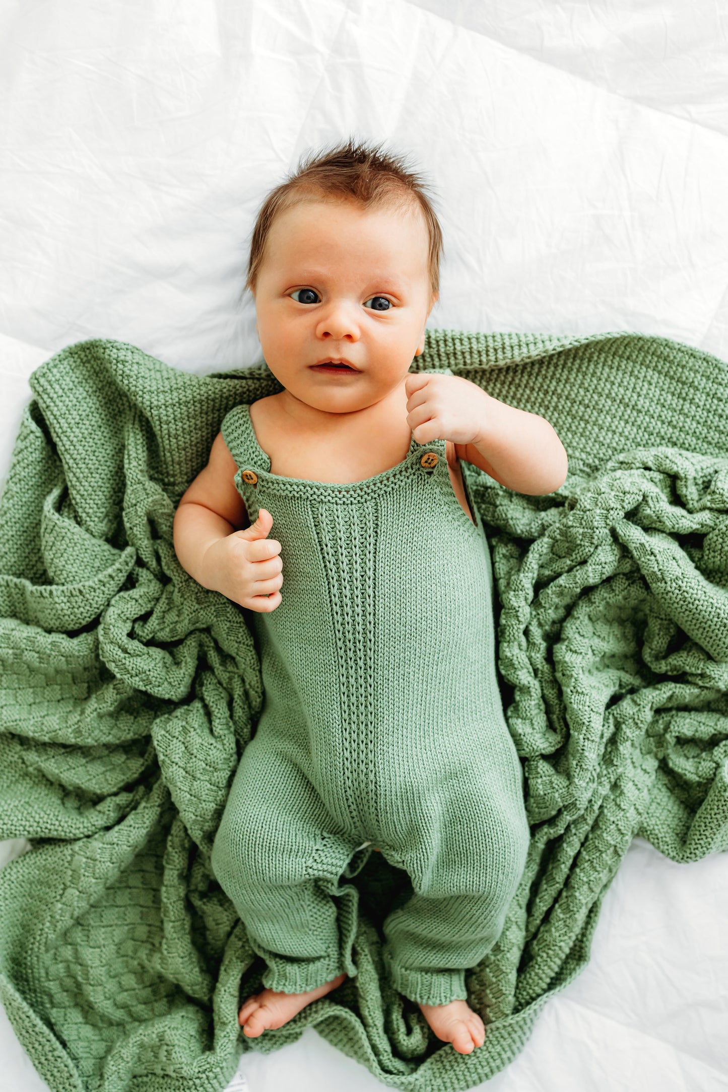 A baby wearing a matching green knitted romper.