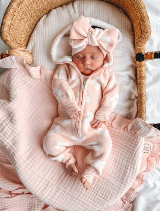A sleeping baby wearing a pink hooded onesie and a bow.
