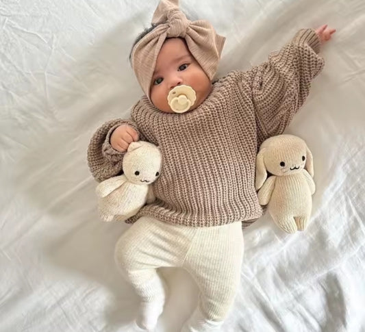 A baby dressed in a knitted brown sweater and cream leggings.