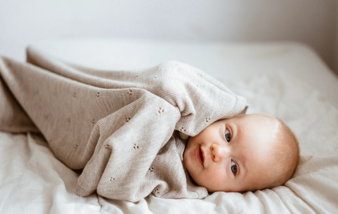 A smiling baby wrapped in a cozy beige blanket.