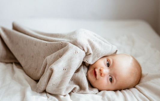 A smiling baby wrapped in a cozy beige blanket.
