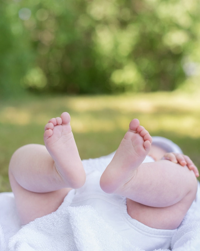 Baby lying on a soft white blanket with feet in focus.