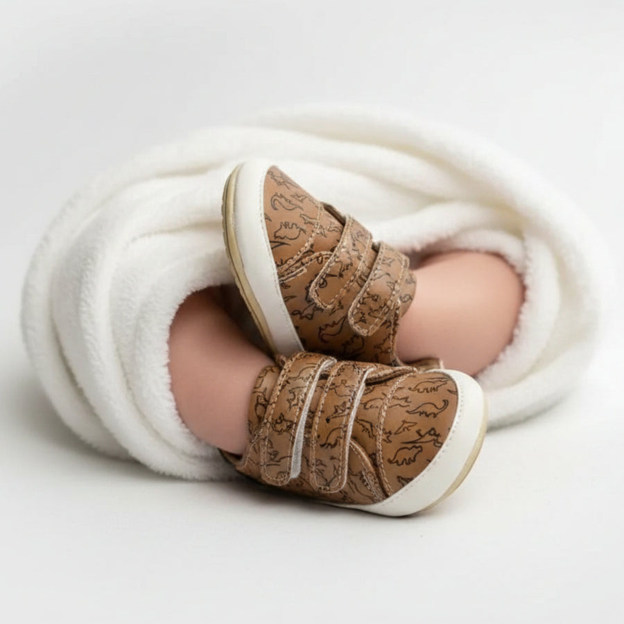 Brown toddler shoes with dinosaur print and Velcro straps.