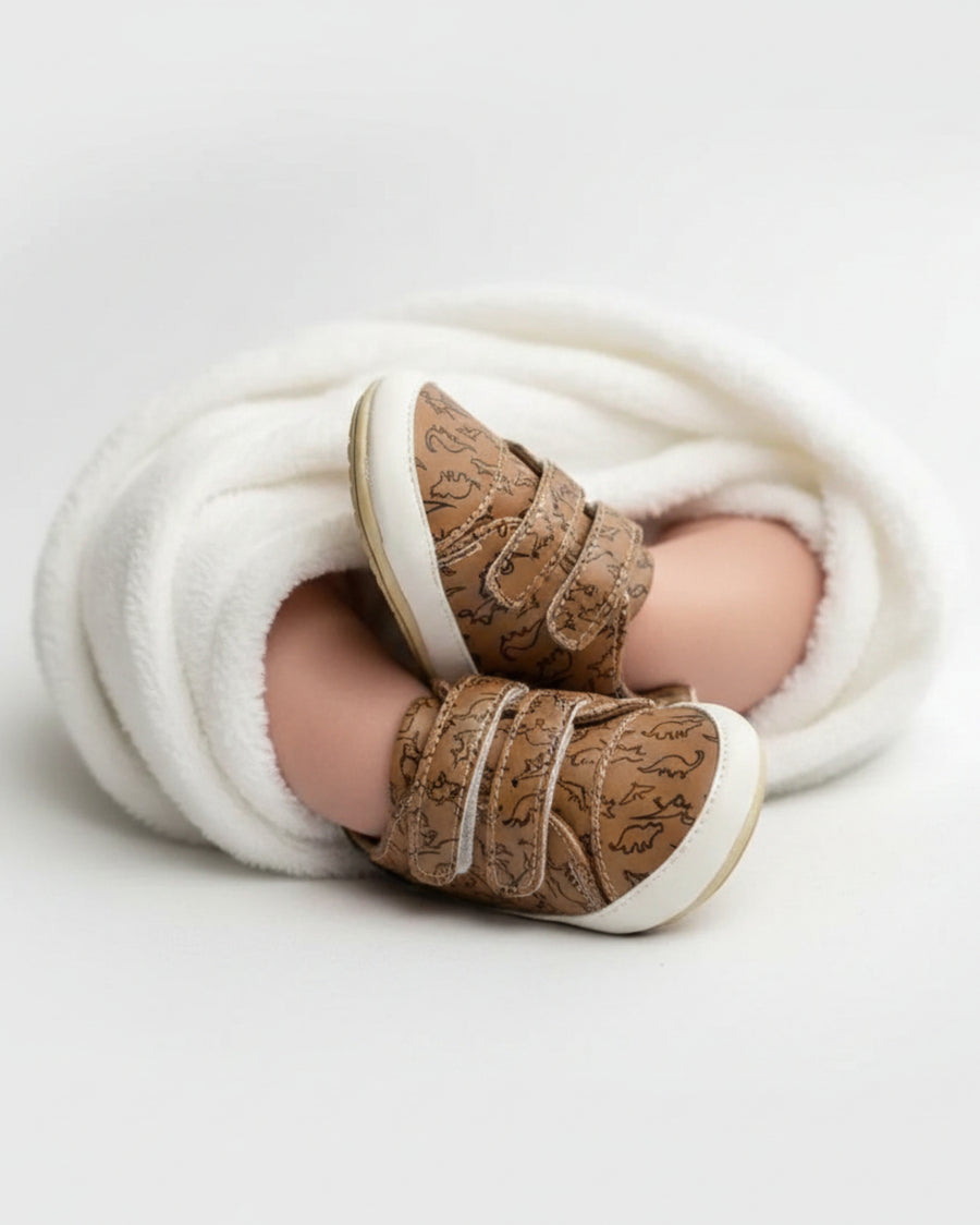 Brown toddler shoes with dinosaur print and Velcro straps.