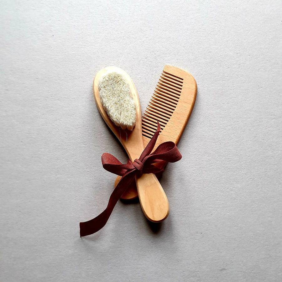 Wooden baby brush and comb set tied with a burgundy ribbon.