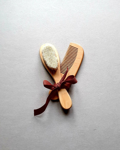 Wooden baby brush and comb set tied with a burgundy ribbon.