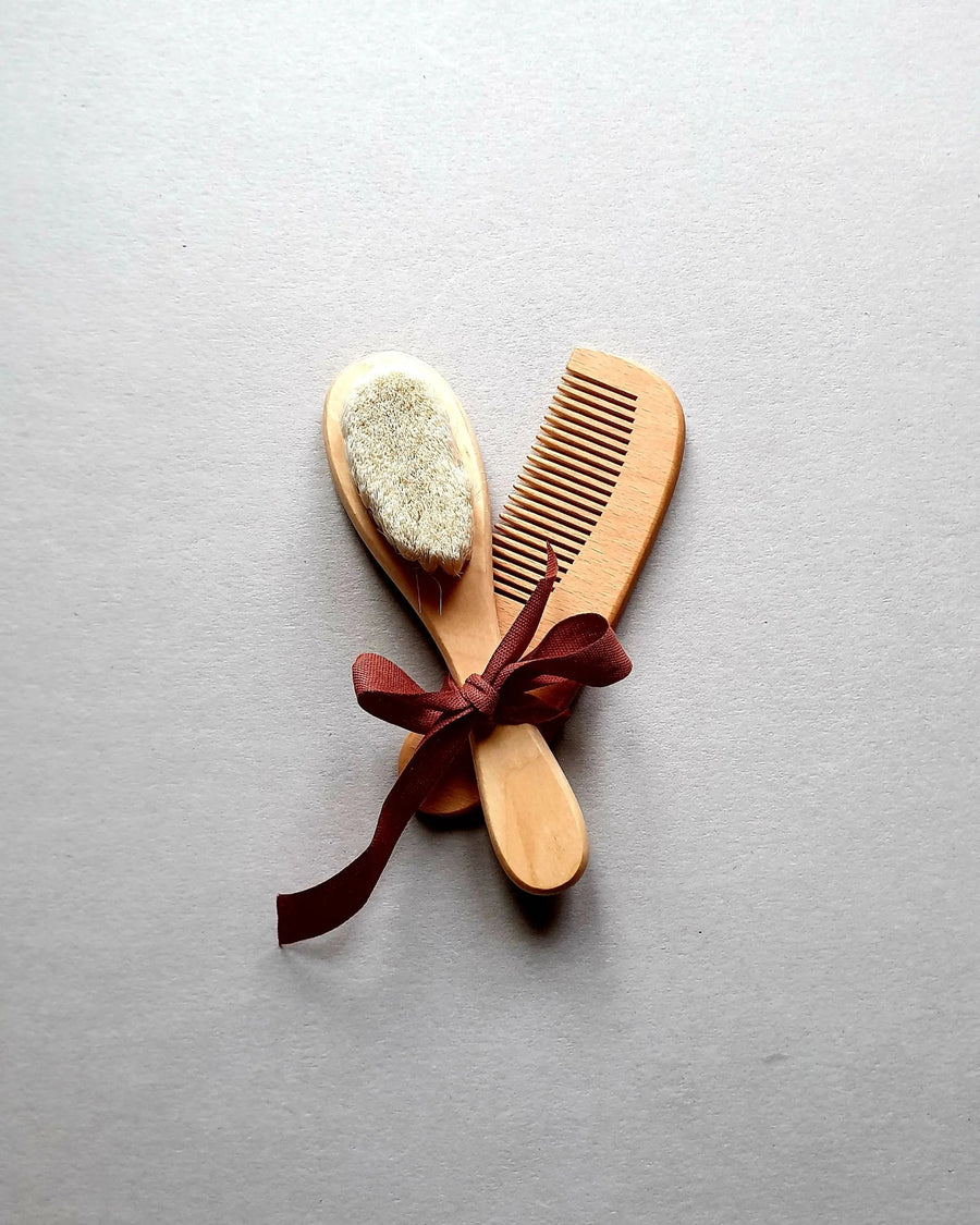 Wooden baby brush and comb set tied with a burgundy ribbon.
