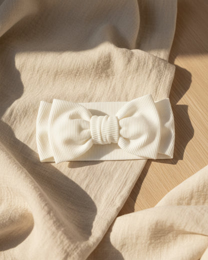 A white, textured fabric headband with a central bow.