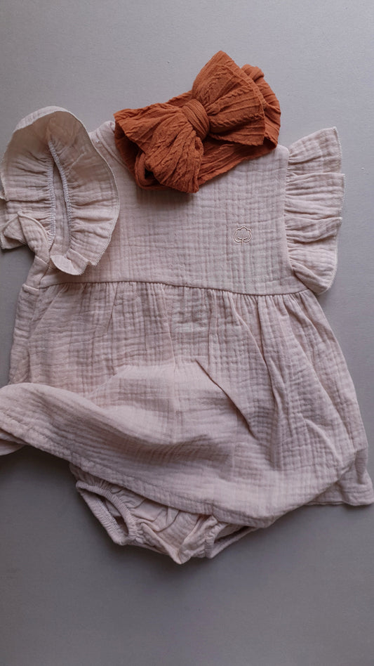 A soft, pale pink baby romper with a brown bow.
