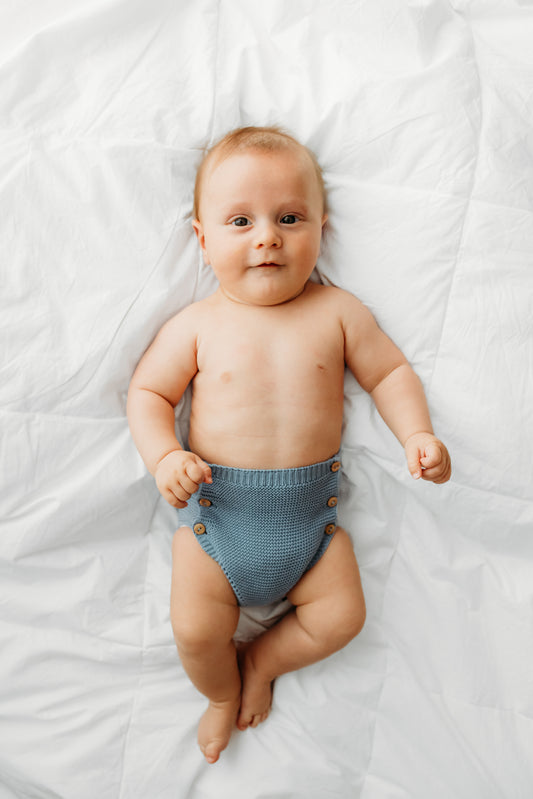A baby wearing blue knitted shorts with buttons.