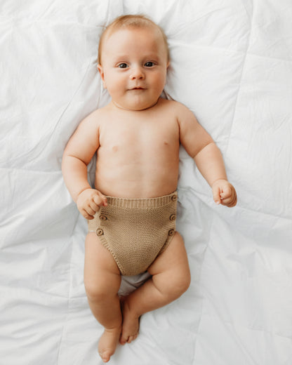 A baby wearing blue knitted shorts with buttons.