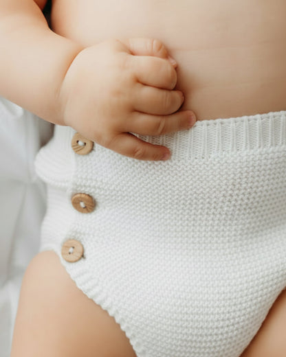A baby wearing knitted blue shorts with wooden buttons.
