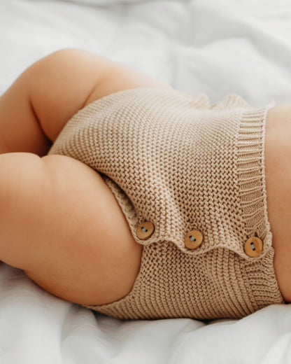 A baby in blue knit shorts with wooden buttons.